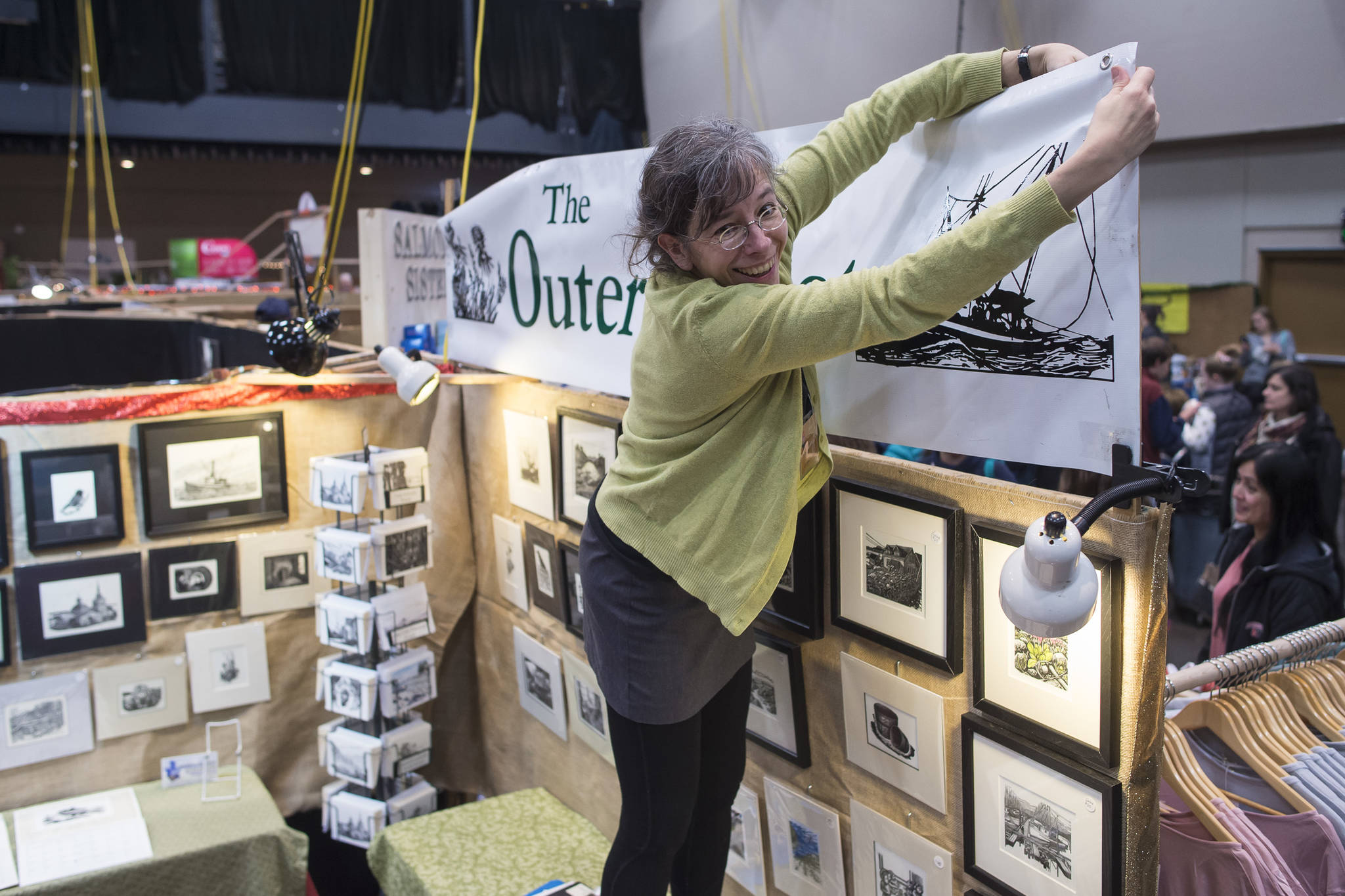 Rebecca Poulson ties up her sign “The Outer Coast” for her prints at the Public Market in Centennial Hall on Friday, Nov. 23, 2018. (Michael Penn | Juneau Empire)