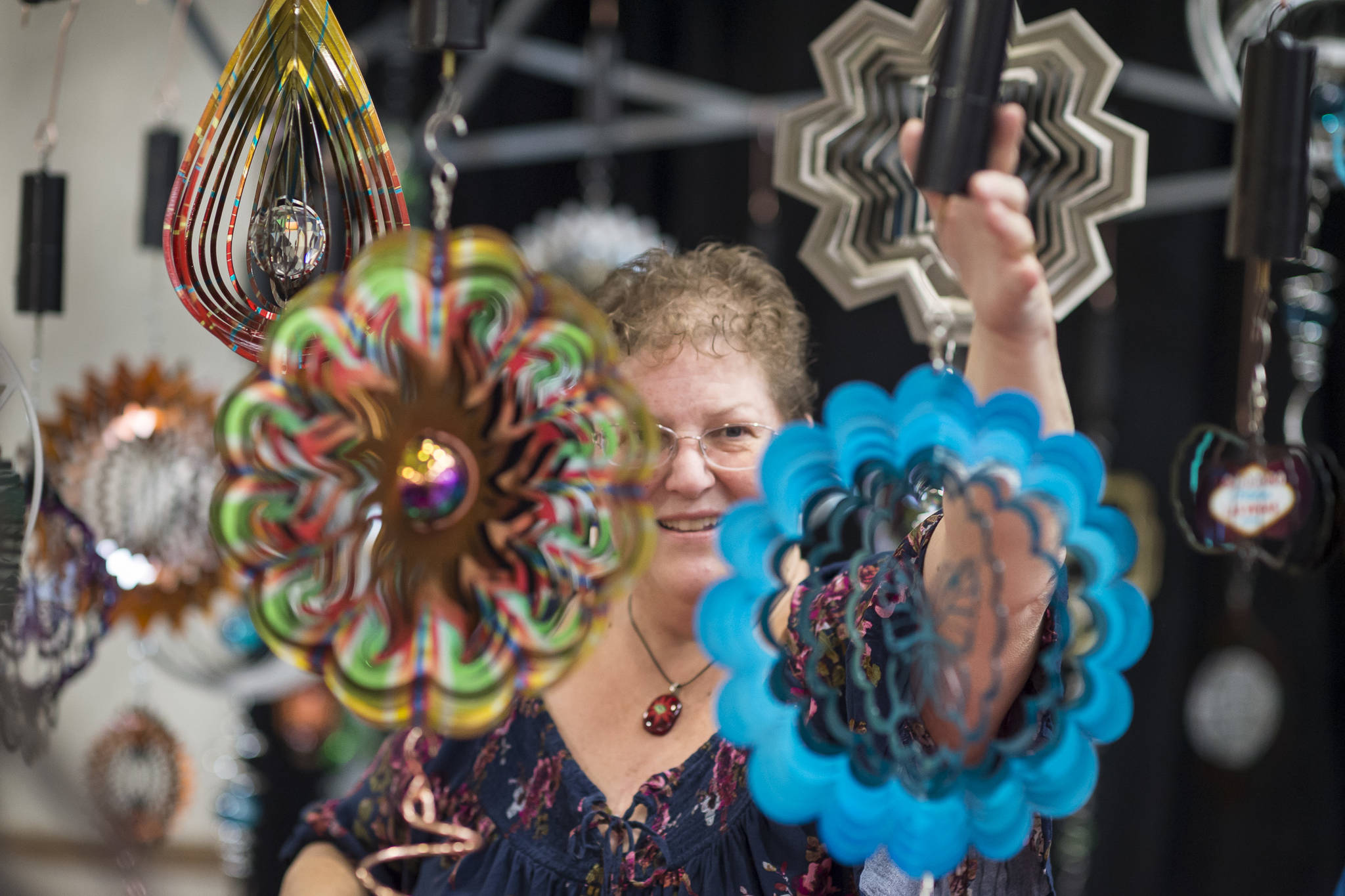 Marla Olsen hangs one of her wind spinners at the display booth she shares with her sister, Ruth, at the Public Market in the Elizabeth Peratrovich Hall on Friday, Nov. 23, 2018. (Michael Penn | Juneau Empire)