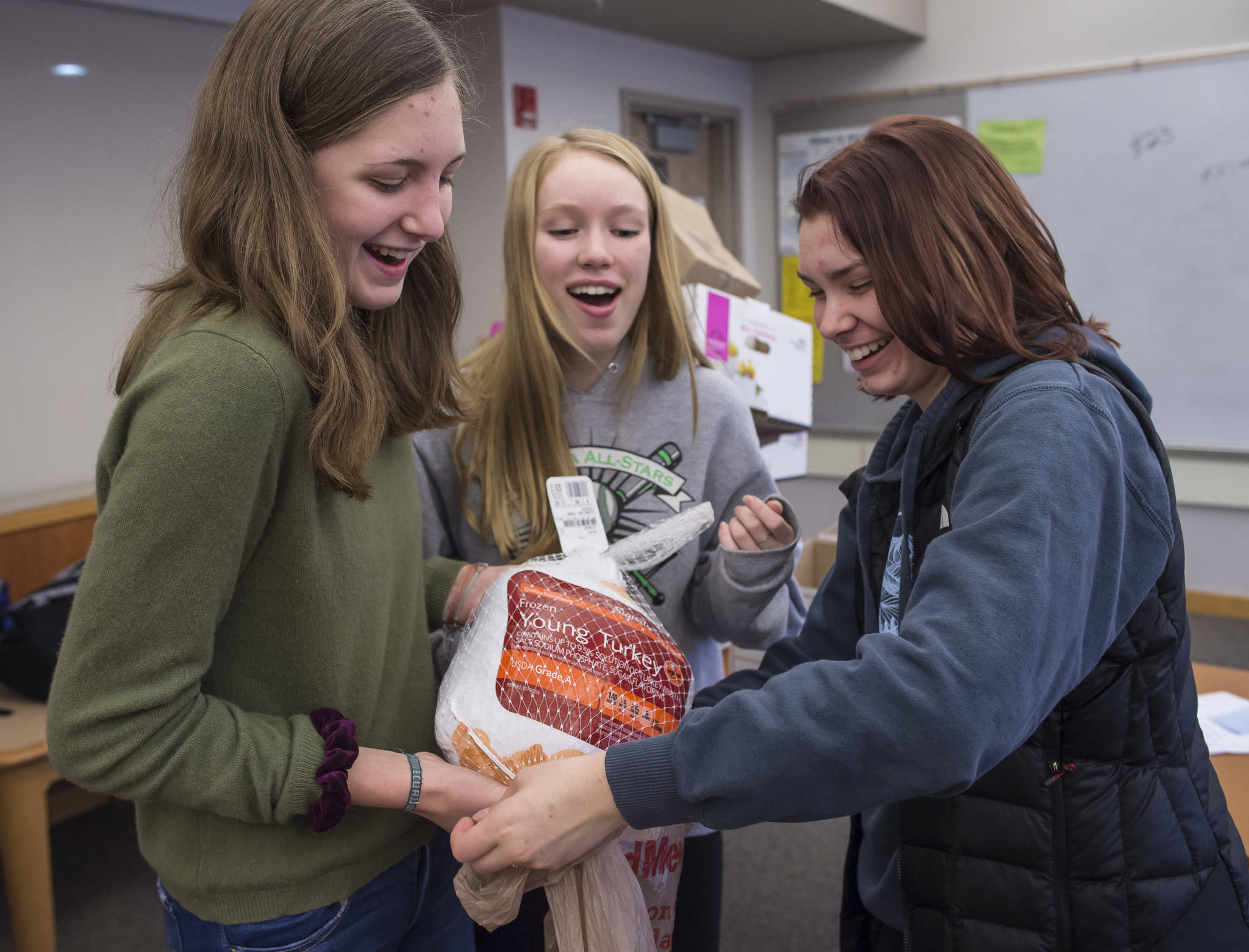 Juneau-Douglas High School freshmen Brooke Sanford, left, Margot Oliver, center, bag a turkey with senior Riley Stadt as they prepare Thanksgiving dinner boxes to be donated to AWARE and The Glory Hall on Tuesday, Nov. 20, 2018. The JDHS chapter of Sources of Strength, a nationwide organization that promotes positivity in schools donated seven boxes to the organizations. Students from every homeroom contributed food. (Michael Penn | Juneau Empire)