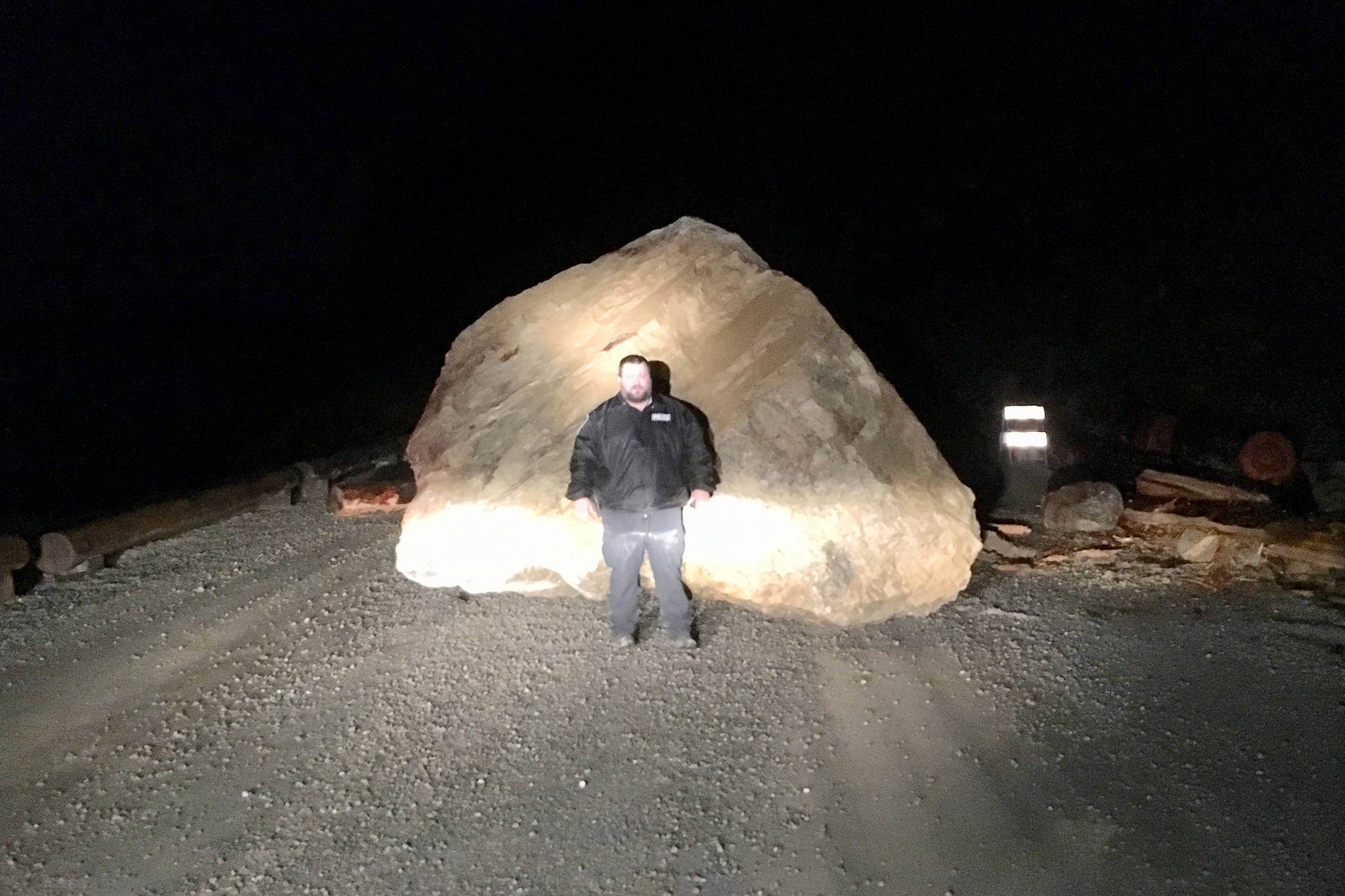 A man poses with a large boulder that fell on a Hoonah road in the early hours of Sunday, Nov. 25, 2018. Nobody was harmed. (Courtesy Photo | Hoonah Volunteer Fire Department)