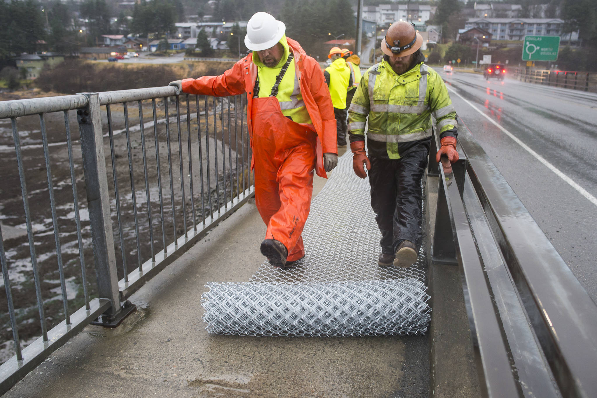 Richard Asplund, left, and Nate Narum, from the Department of Transportation and Public Facilities, roll out chain-link fencing before installation along the pedestrian walkway over the Douglas Bridge on Monday, Nov. 26, 2018. (Michael Penn | Juneau Empire)