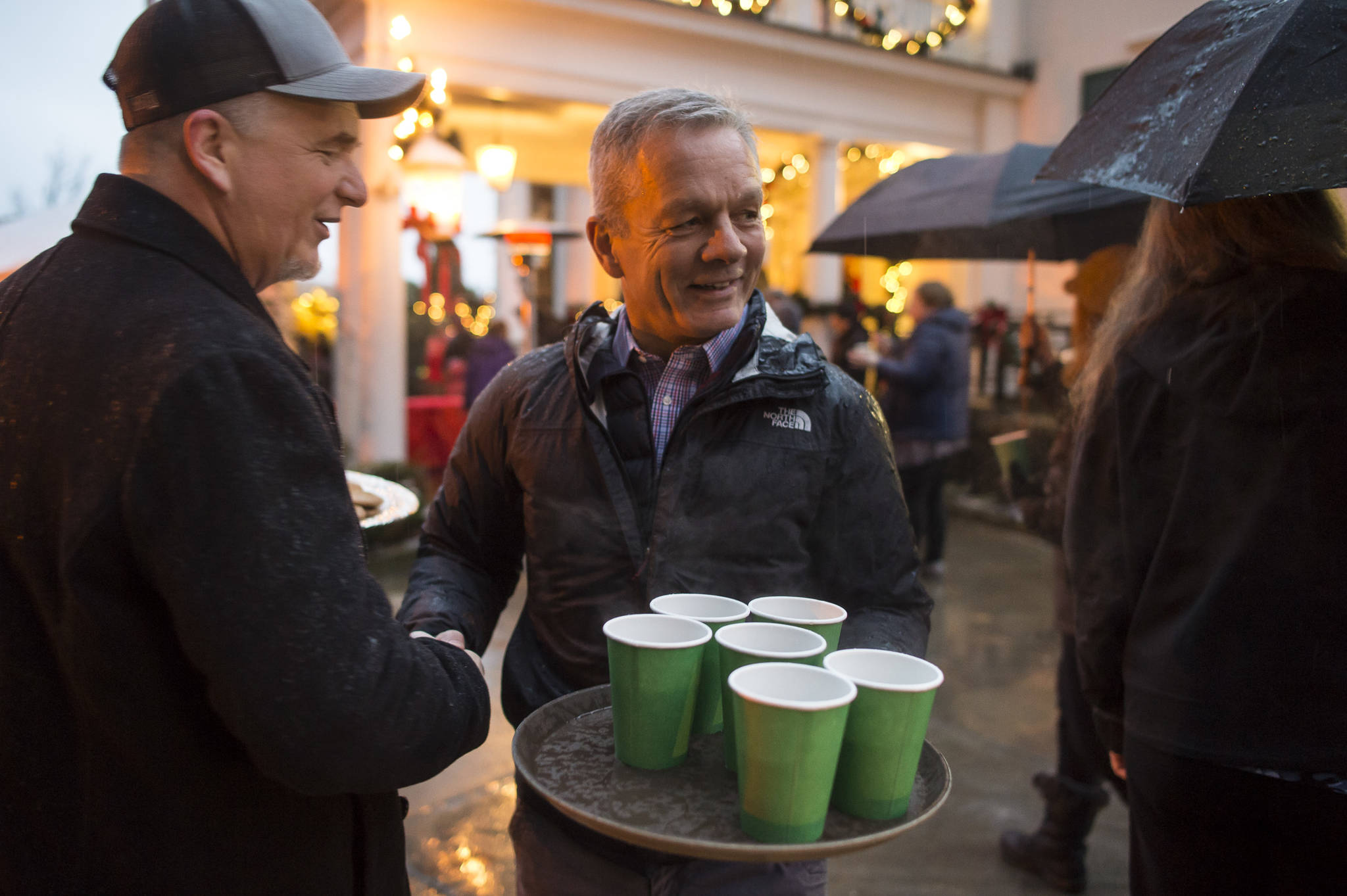 Special advisor Ben Stevens, center, and Legislative Liaison for the Department of Transportation and Public Facilities Mike Lesmann, left, serve cookies and cider to Juneau residents waiting at the Governor’s Open House on Tuesday, Dec. 11, 2018. (Michael Penn | Juneau Empire)