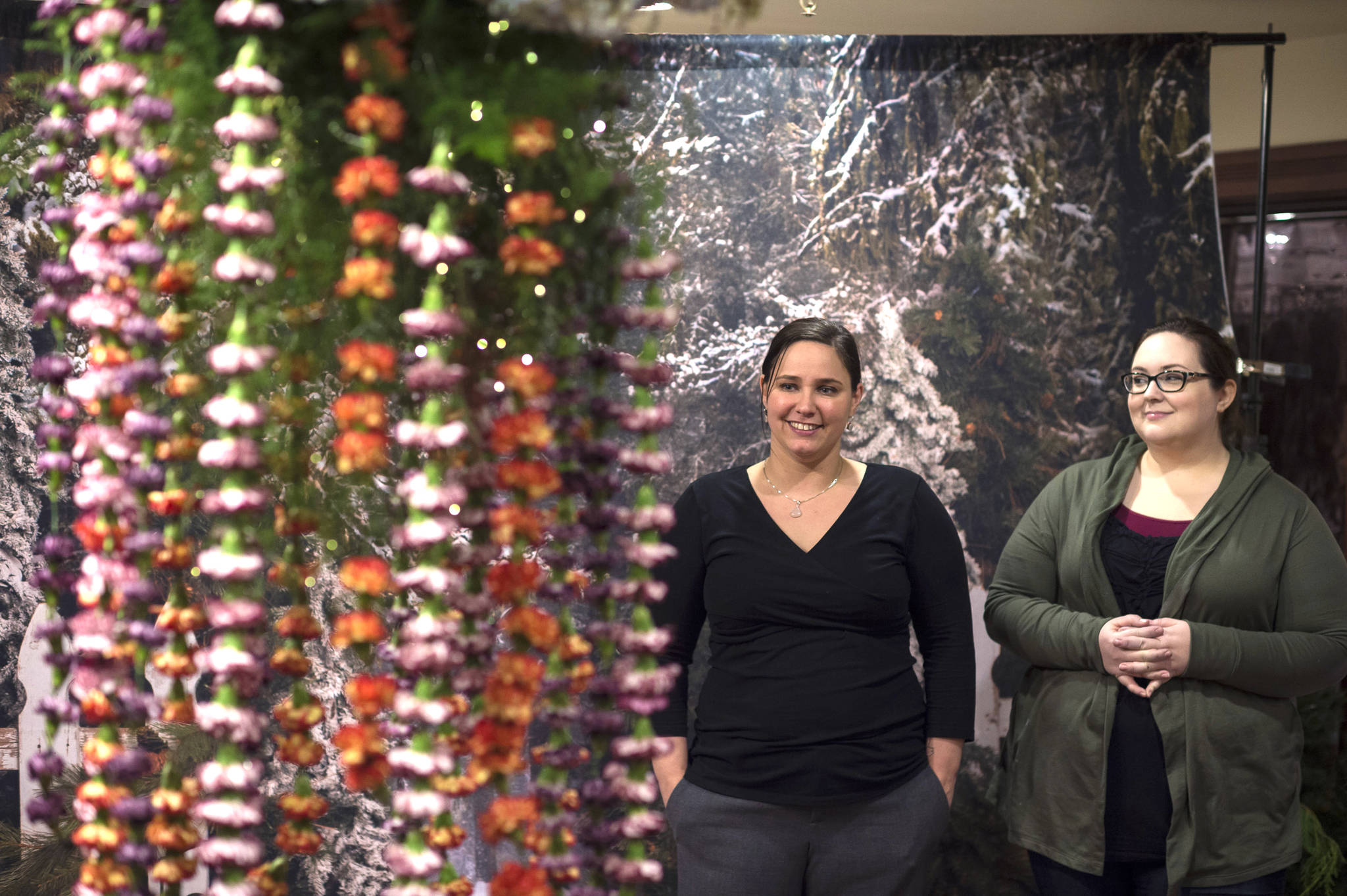 Kimberlee Wear, owner of Captive Moments Alaska, right, and Debrah Clements, owner of Martha’s Flowers, admire Clements’ hanging flower display in the Senate Building during Gallery Walk on Friday, Dec. 7, 2018. (Michael Penn | Juneau Empire)