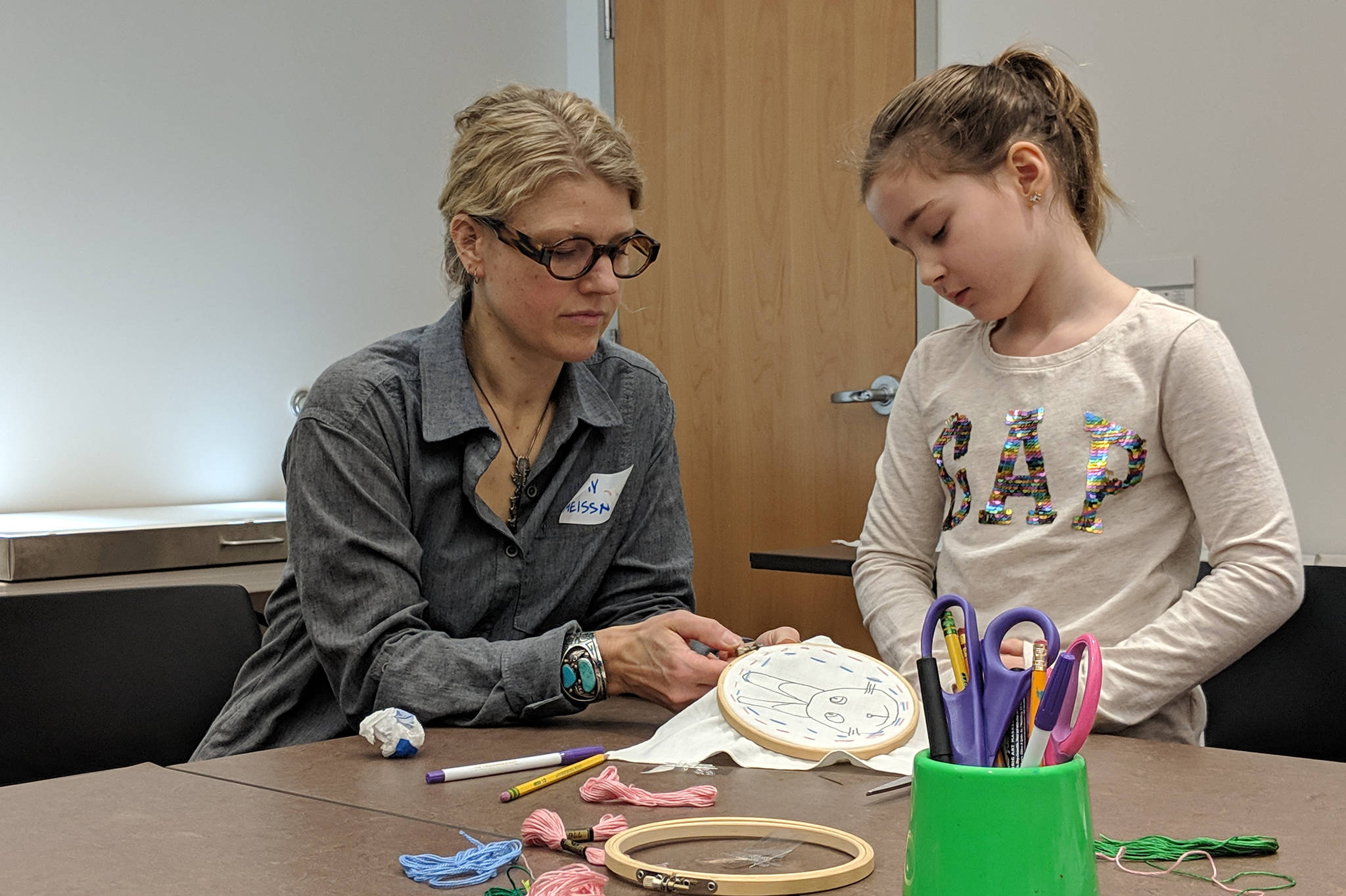 Artist Amy Meissner works with Ellinore Higgins, 7, during an embroidery activity for kids Saturday, Dec.8, 2018 at the Alaska State Library, Archives and Museum. (Ben Hohenstatt | Capital City Weekly)