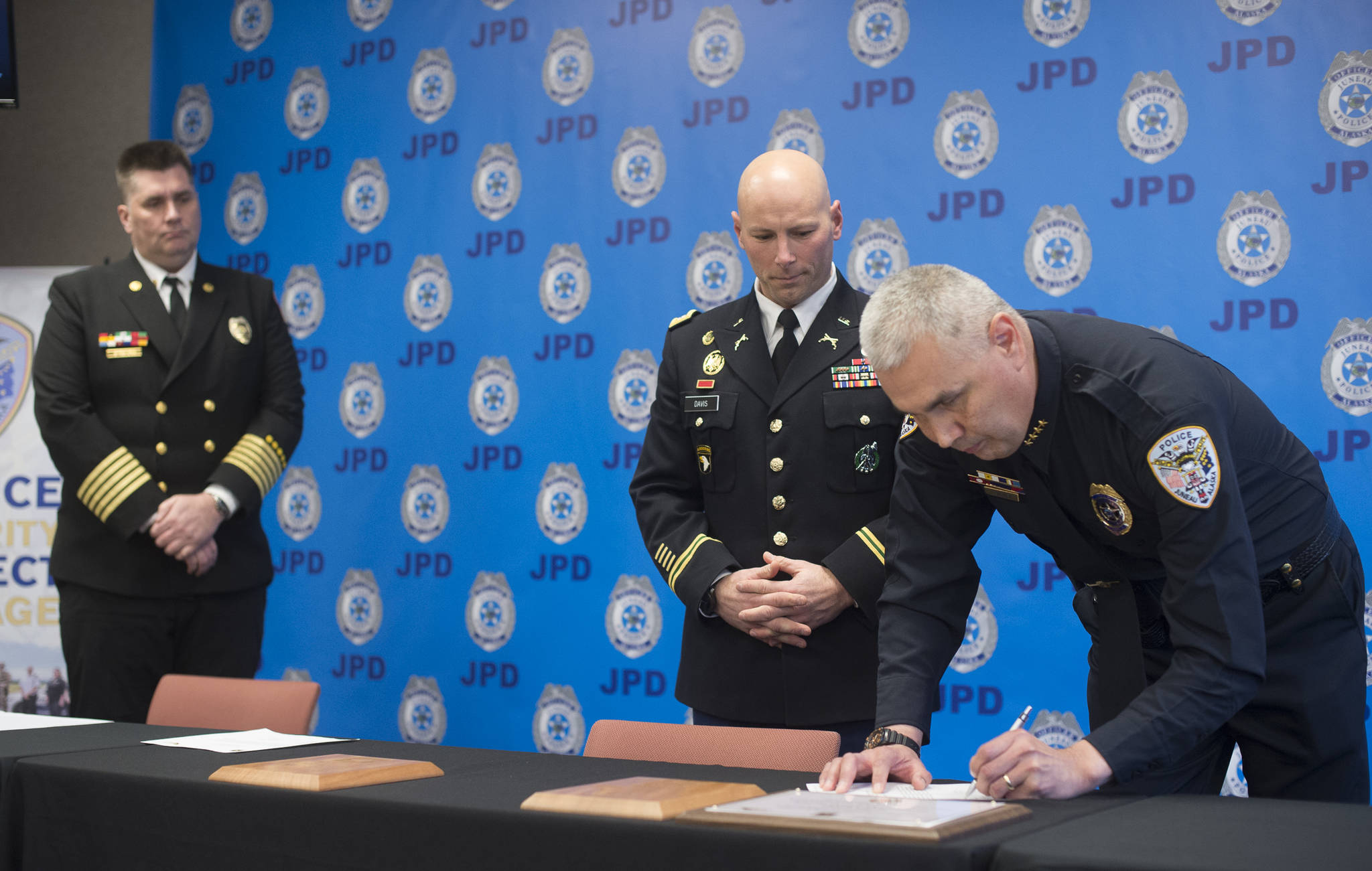 Lt. Colonel Mark A. Davis, battalion commander, Seattle Recruiting Battalion, center, watches as Juneau Police Department Chief Ed Mercer, right, and Capital City Fire/Rescue Chief Richard Etheridge take turns signing a partnership between JPD, CCFR and the U.S. Army at the Juneau Police Station on Wednesday, Dec. 12, 2018. The The Partnership for Youth Success (PaYS) Program helps soldiers getting ready to leave the military find employment. (Michael Penn | Juneau Empire)