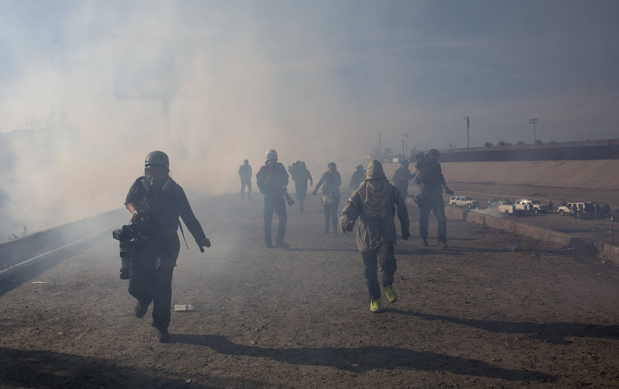 Migrants run from tear gas launched by U.S. agents, amid photojournalists covering the Mexico-U.S. border, after a group of migrants got past Mexican police at the Chaparral crossing in Tijuana, Mexico, Sunday, Nov. 25, 2018. The mayor of Tijuana has declared a humanitarian crisis in his border city and says that he has asked the United Nations for aid to deal with the approximately 5,000 Central American migrants who have arrived in the city. (AP Photo | Rodrigo Abd)