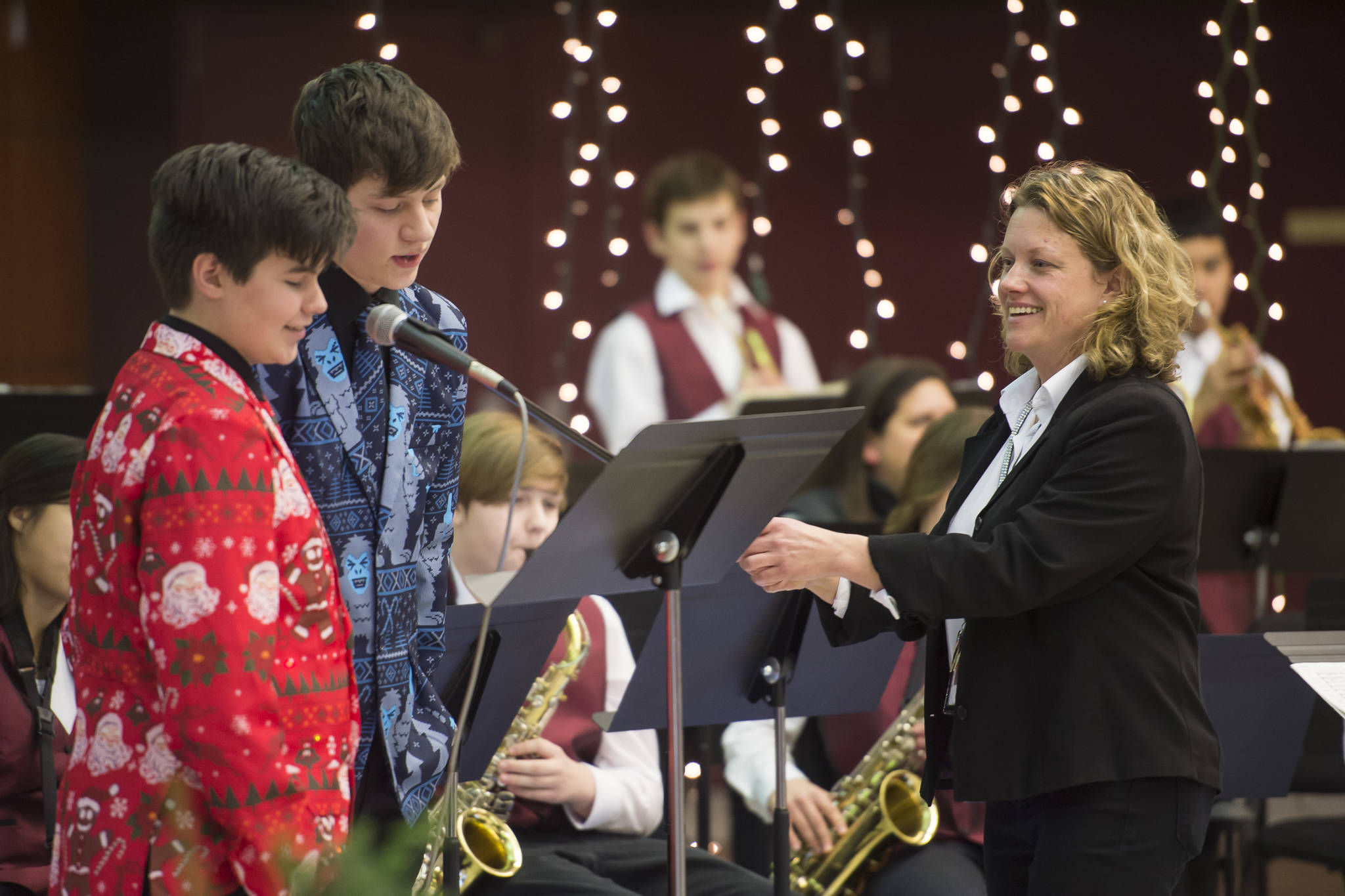 Band Director Amy Bibb adjusts the microphone as freshman Toby Russell, left, and senior Dakota Morgan sing with the Juneau-Douglas High School Jazz Band during a holiday music concert at JDHS on Thursday, Dec. 13, 2018. (Michael Penn | Juneau Empire)