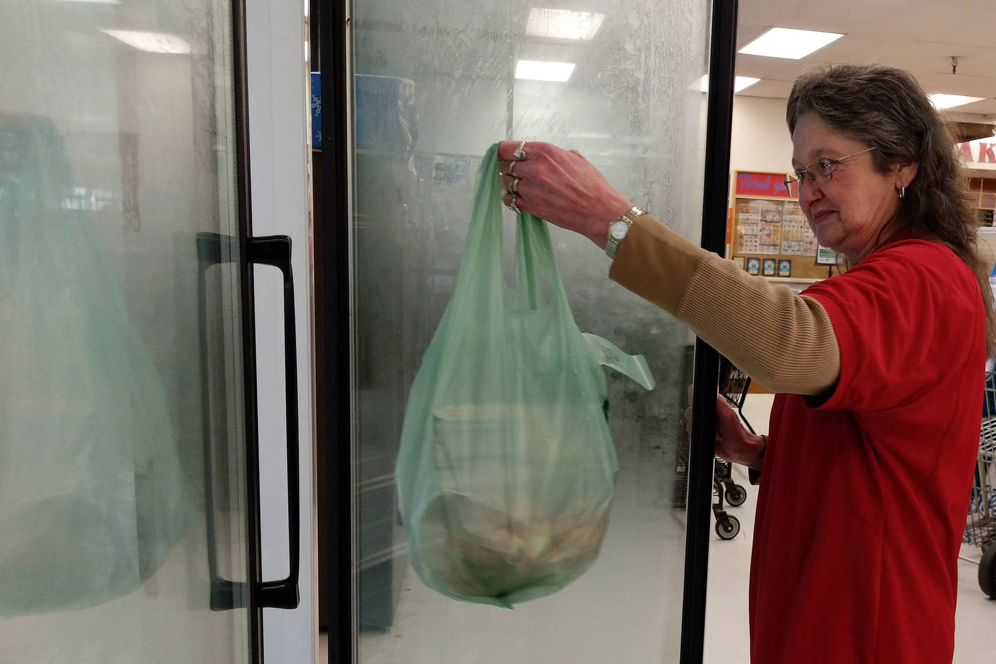 Mary Lou Stone, supervisor for Super Bear Supermarket IGA, puts a bag of groceries ready for pickup in a cooler near the front of the store on Thursday, Dec. 27, 2018. Super Bear Supermarket IGA is part of a trend toward increased availability of online grocery shopping. (Ben Hohenstatt | Juneau Empire)