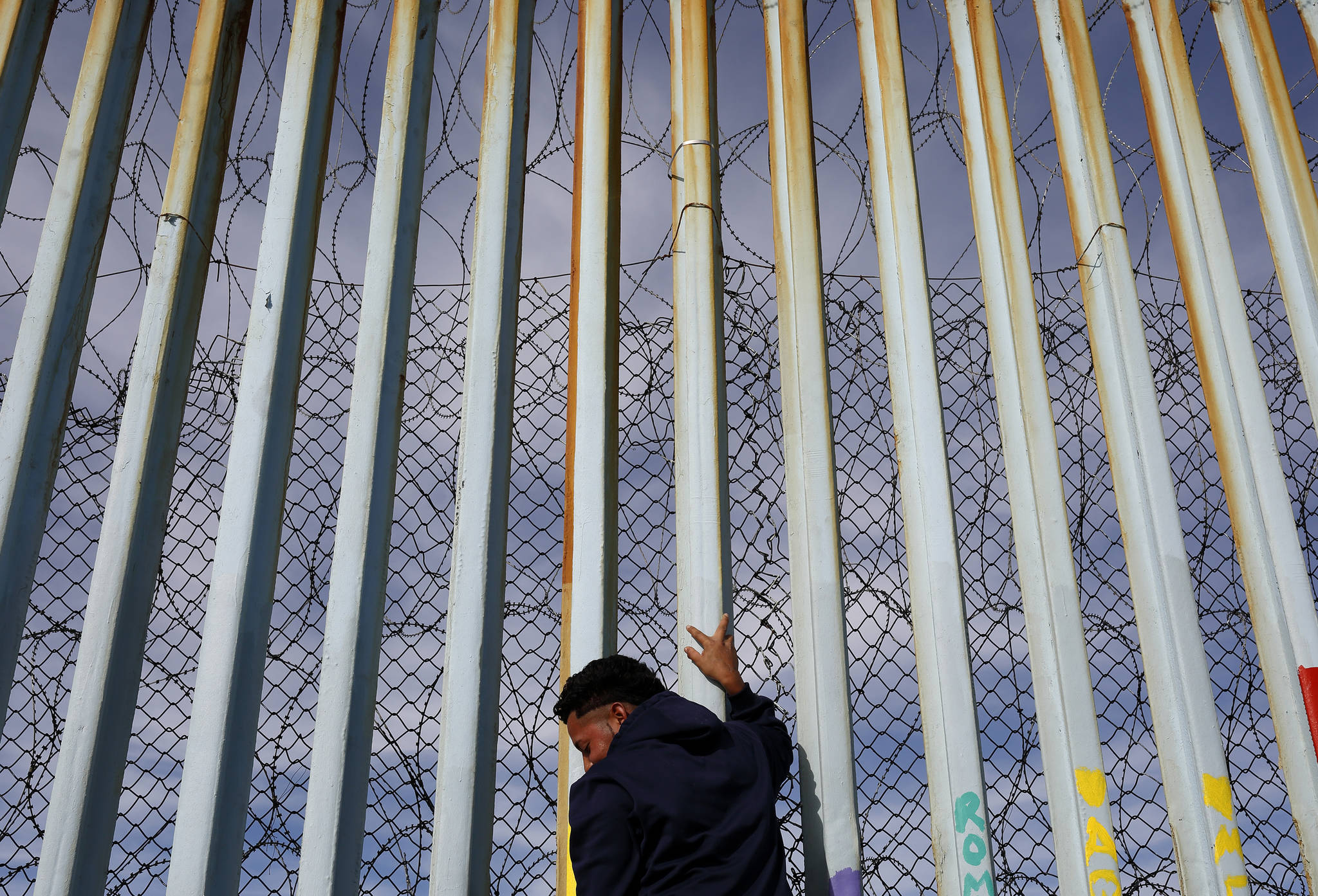 In this Jan. 8, 2019 photo, a man holds on to the border wall along the beach, in Tijuana, Mexico. The migrant caravan that was seized upon by U.S. President Donald Trump in the run-up to the 2018 election has quietly dwindled to a few hundred people, with many of them having crossed into the U.S. or put down roots in Mexico. (Gregory Bull | Associated Press)