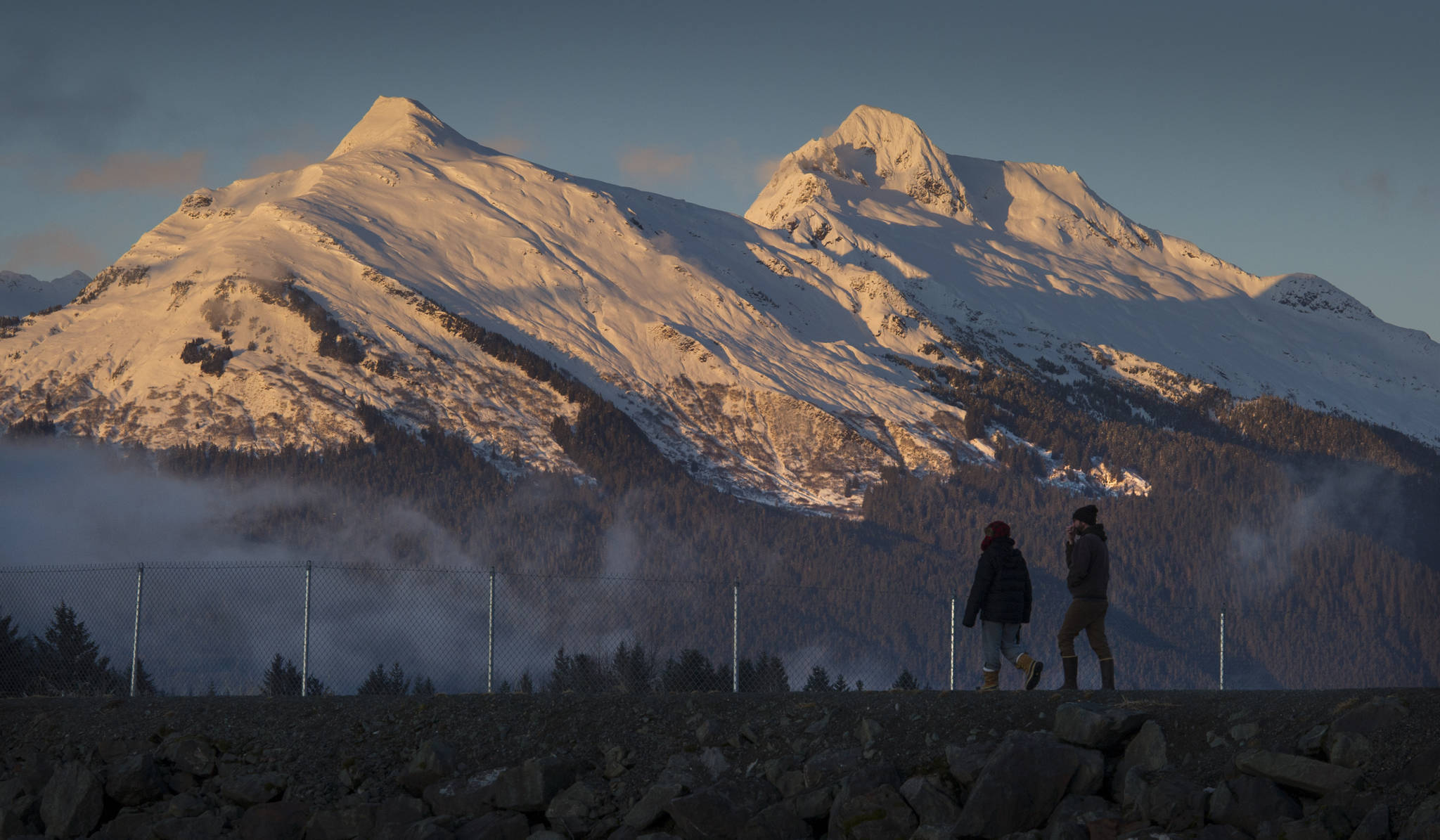 In this Jan. 8, 2018 photo, a couple walks along the Airport Dike Trail as the evening light shines on Mt. McGinnis, left, and Stroller White Mountain. (Michael Penn | Juneau Empire File)