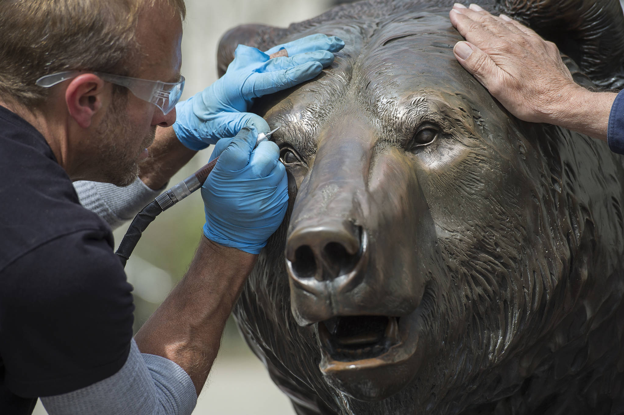 Sculpture artist R.T. “Skip” Wallen and patineur Bart Latta, of the Parks Bronze foundry in Enterprise, Oregon, work to give Wallen’s bronze bear sculpture, Windfall Fisherman, a 30-year cleanup on Main Street on Thursday, May 10, 2018. Wallen and Latta were etching details that have worn off since it was installed in 1988. Wallen said the work is “making a friendlier bear out of it. That’s part of the expression that has bothered me for 30 years.” (Michael Penn | Juneau Empire)