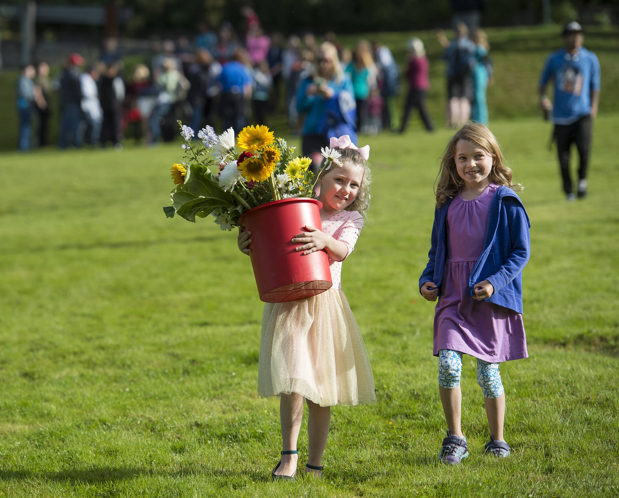 Juneau Community Charter School second-grader Elianna Amati, left, carries her class’s flowers with third-grader Rebecca Frank after a ceremony at Evergreen Cemetery on the first of the school year on Monday, Aug. 20, 2018. (Michael Penn | Juneau Empire)