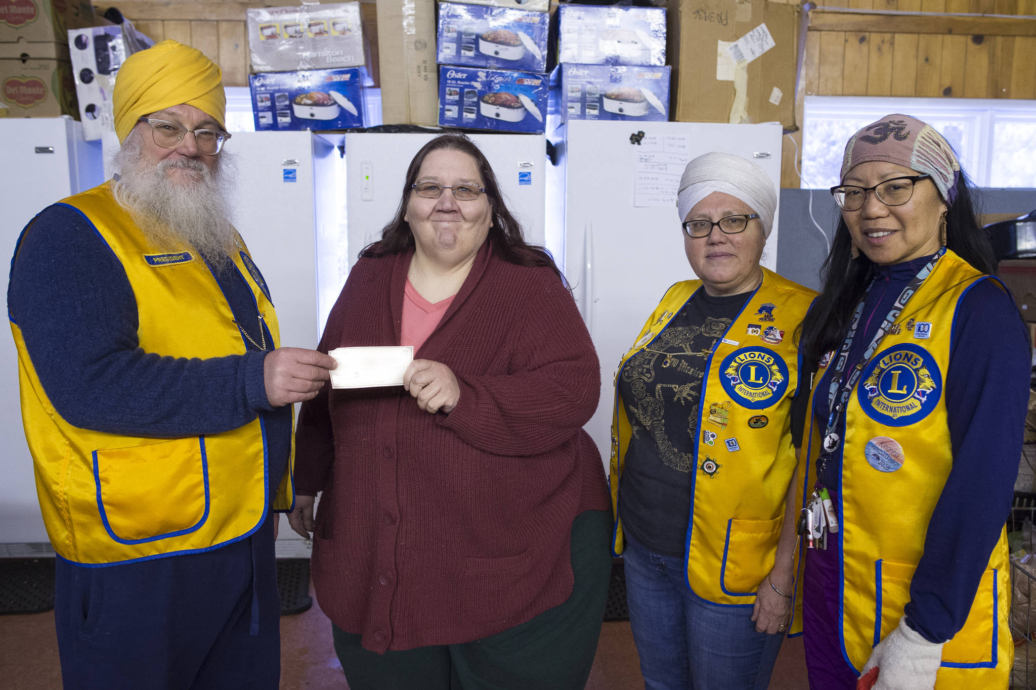 Hari Dev Khalsa, left, President of the Mendenhall Flying Lions Club, his wife, Mukhya Khalsa, second from right, and Nartej Garcia, right, present Karen Fortwengler of Helping Hands of Alaska with a check for $400 at the food bank office in Switzer Village on Friday, Jan. 11, 2019. Along with the money, club members donate about 80 hours a week to help gather and distribute food. The food bank is open for distribution Tuesday and Friday 5:30-6:50 p.m. (Michael Penn | Juneau Empire)