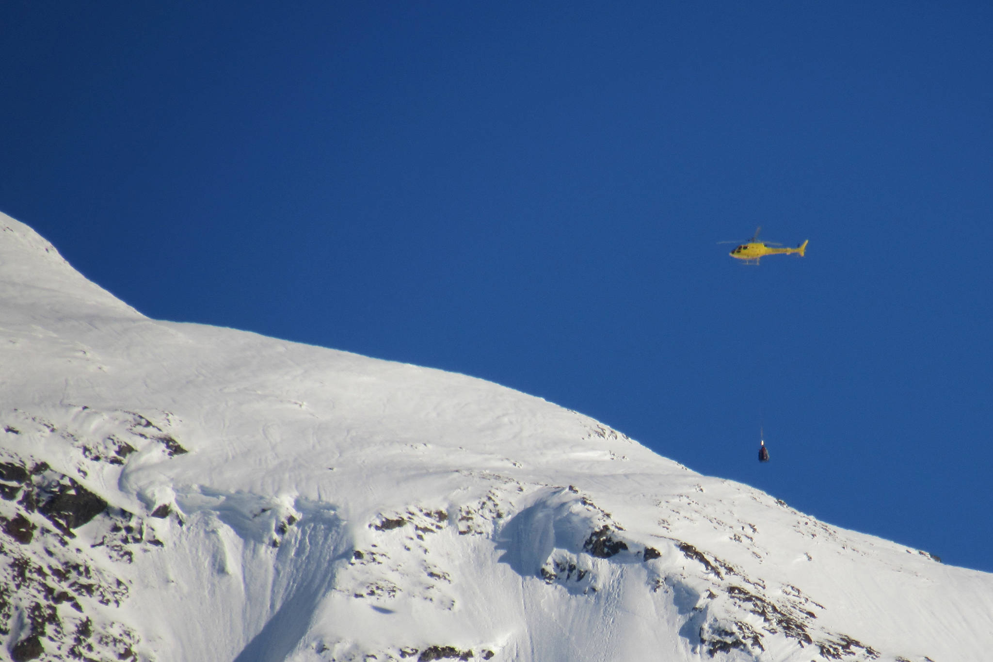A yellow helicopter buzzes around Mount Roberts with a piece of avalanche mitigation equipment known as a DaisyBell, Thursday, Jan. 17, 2019. No major avalanches were triggered. (Ben Hohenstatt | Juneau Empire)