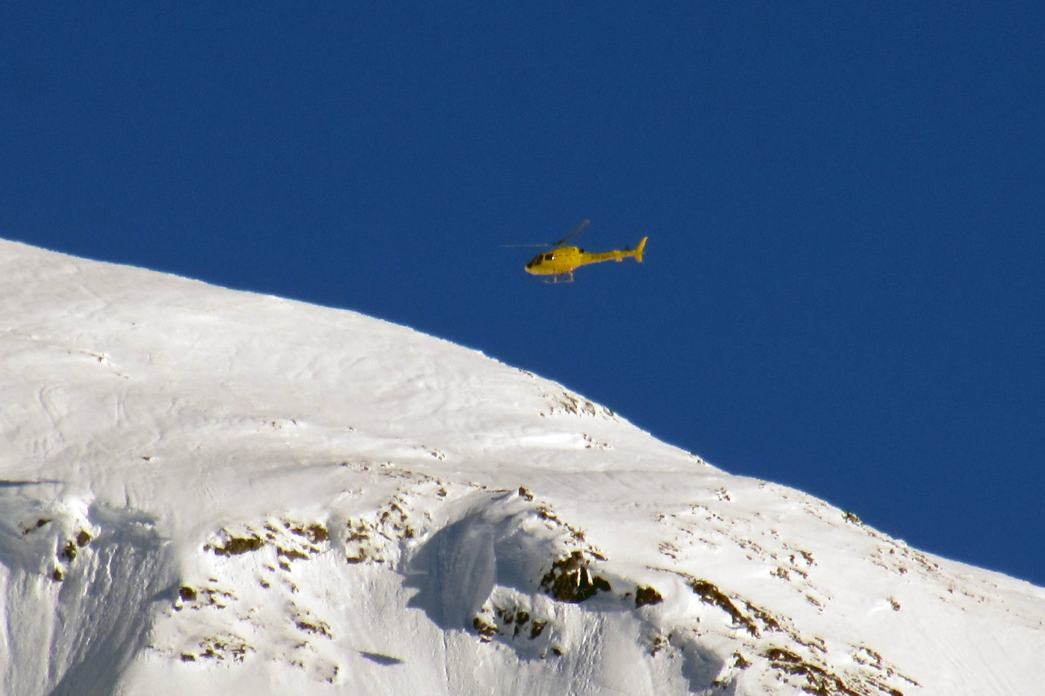 A yellow helicopter buzzes around Mount Roberts with a piece of avalanche mitigation equipment known as a DaisyBell, Thursday, Jan. 17, 2019. (Ben Hohenstatt | Juneau Empire)