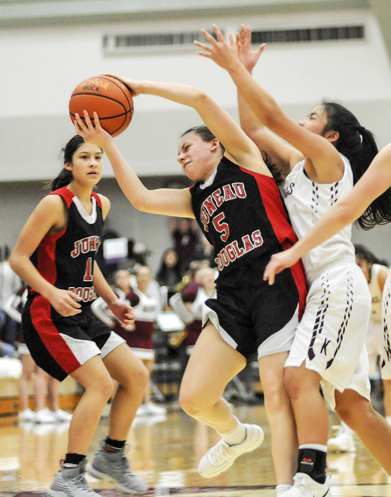 Juneau-Douglas player Trinity Jackson, left watches as teammate Kiana Potter, center, snags a rebound while Kayhi’s Shaelynn Mendoza gets involved in the play. JDHS won 50-35. (Hall Anderson | Ketchikan Daily News)