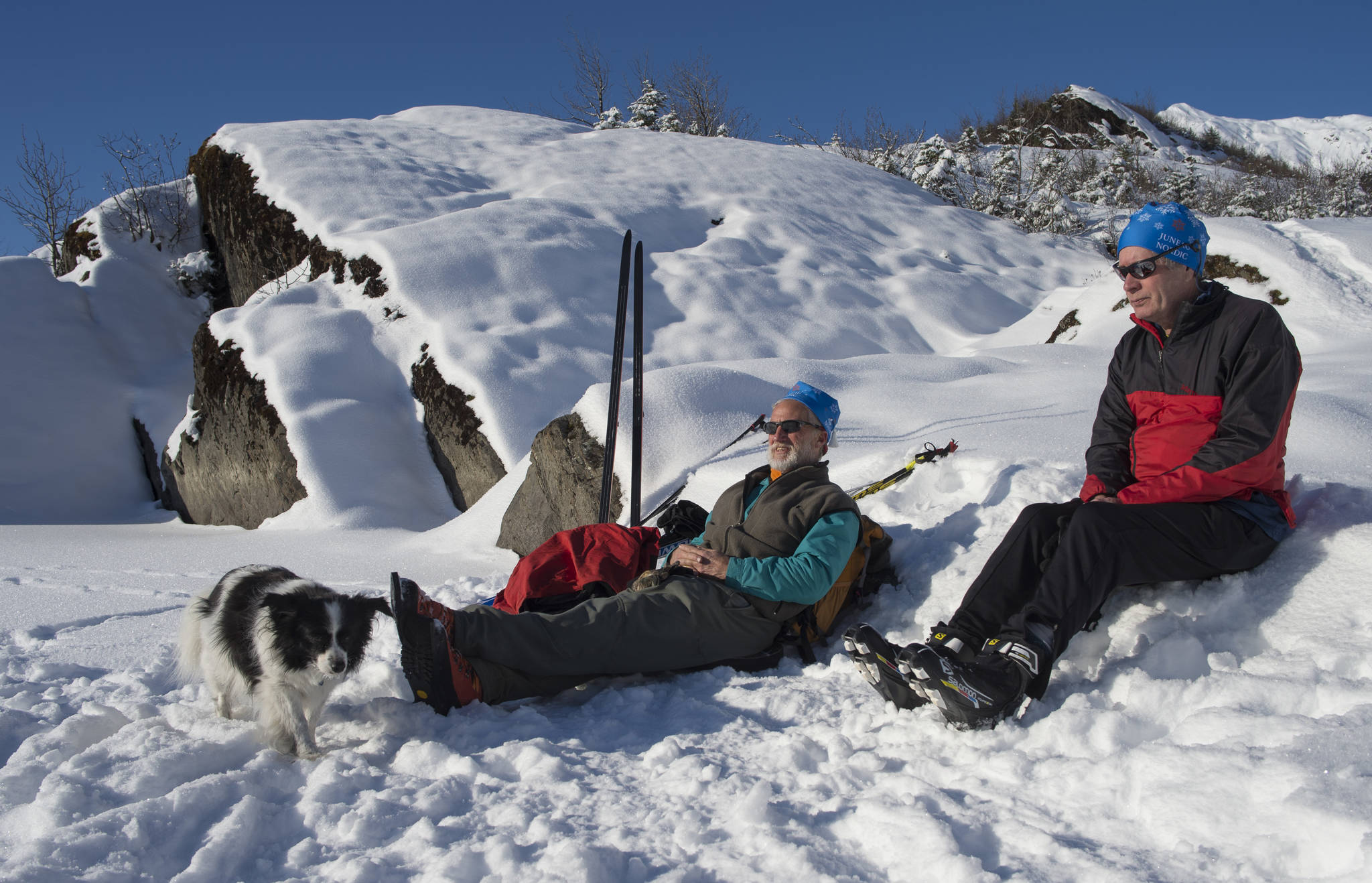 Greg Cook, with his dog, Hibou, and Dr. John Connolly relax in the sun while out skiing at Mendenhall Lake on Monday, Feb. 11, 2019. (Michael Penn | Juneau Empire)