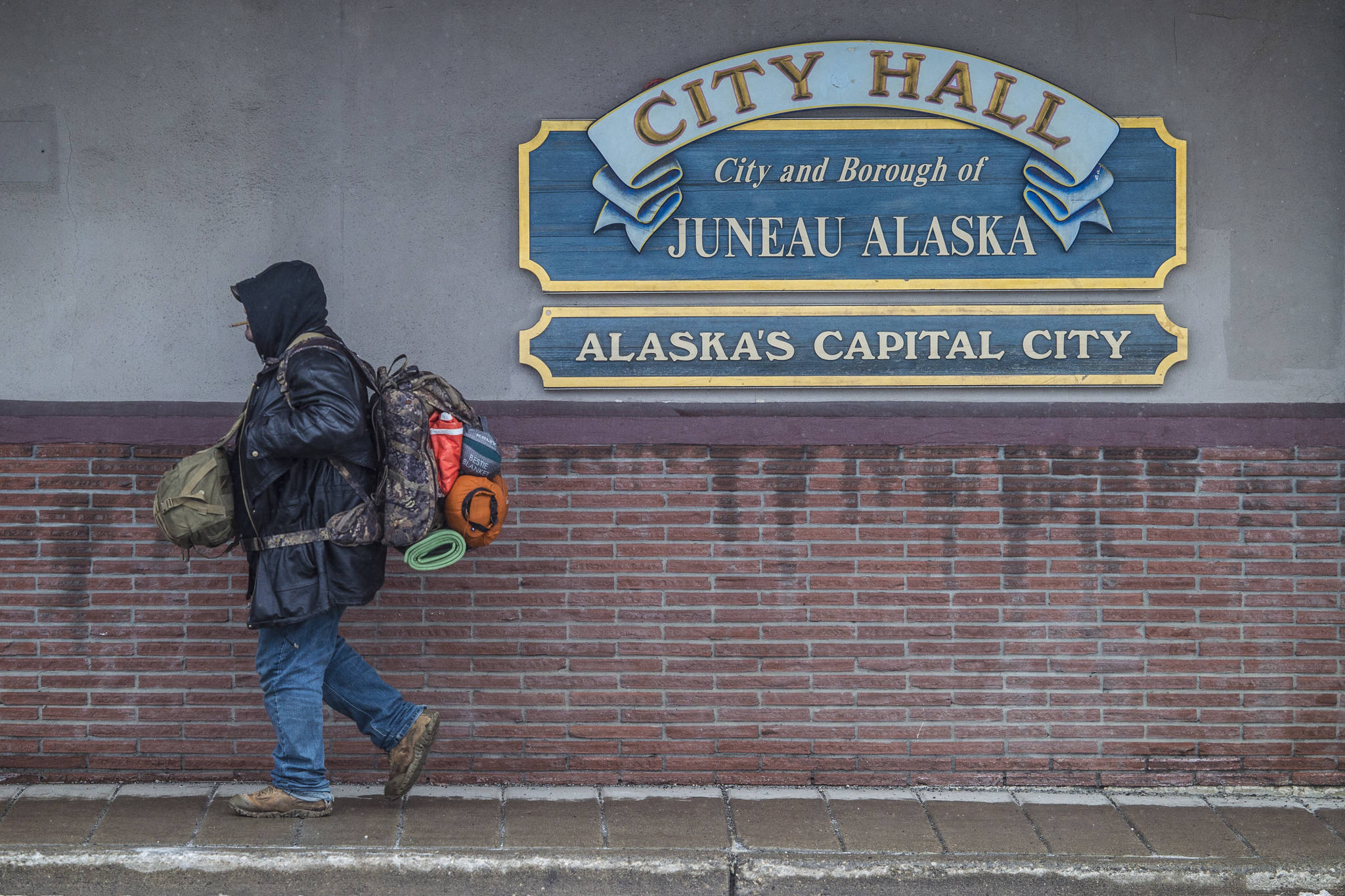 A man with camping gear walks by City Hall on Tuesday, Feb. 12, 2019. Leaders of organizations addressing homelessness have expressed concerns about how state budget cuts will affect their funding for the homeless. (Michael Penn | Juneau Empire)