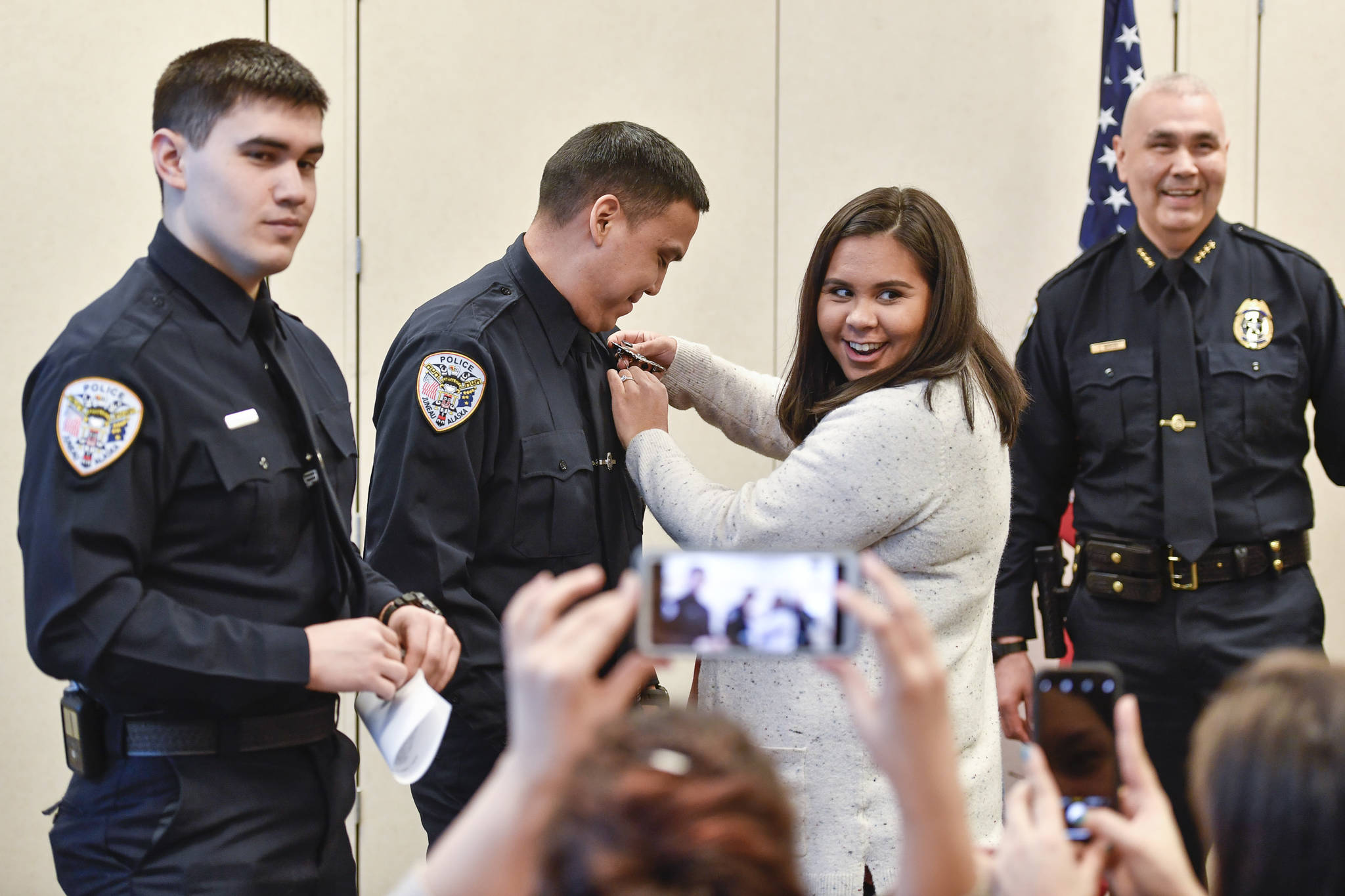 Amber White laughs as she pins a badge on her husband, Duain White, of Juneau, center, during a ceremony for new officers at the Juneau Police Department station on Thursday, Feb. 21, 2019. Chief of Police Ed Mercer, right, swore in White and Jonah Hennings-Booth, of Eagle River, left. (Michael Penn | Juneau Empire)
