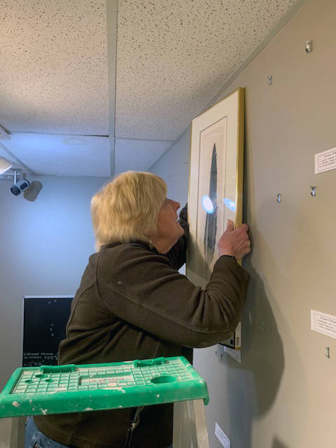 Laurie Craig hangs a work depicting an eagle feather during February before the space’s March 1 grand reopening. (Courtesy Photo | Juneau Artists Gallery)