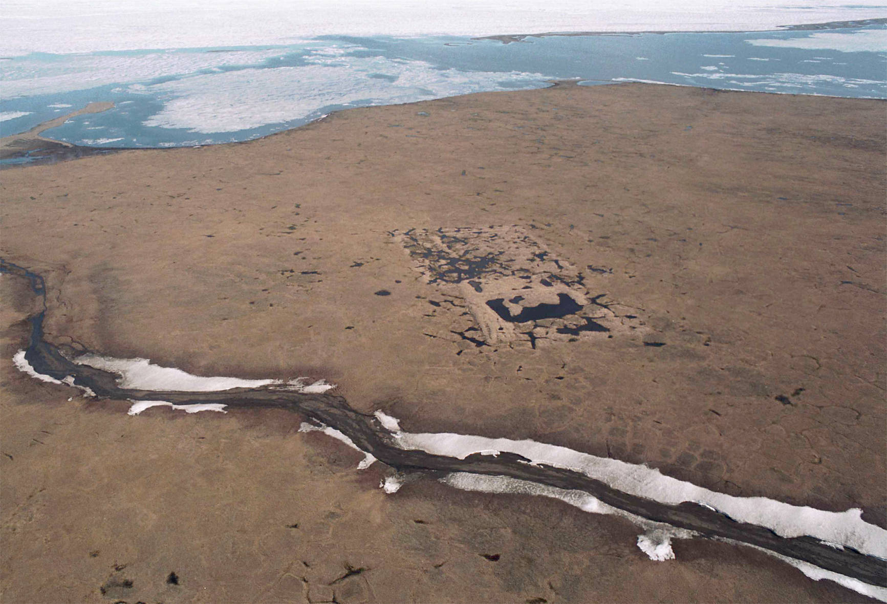 In this file photo, an aerial shows the footprint of the test well drilled in the mid-1980s on land owned by the Kaktovik Native village corporation within the 1002 area of the Arctic National Wildlife Refuge. The well is 14 miles east of Kaktovik and the melting the Beaufort Sea is at the top of the picture. (Michael Penn | Juneau Empire File)