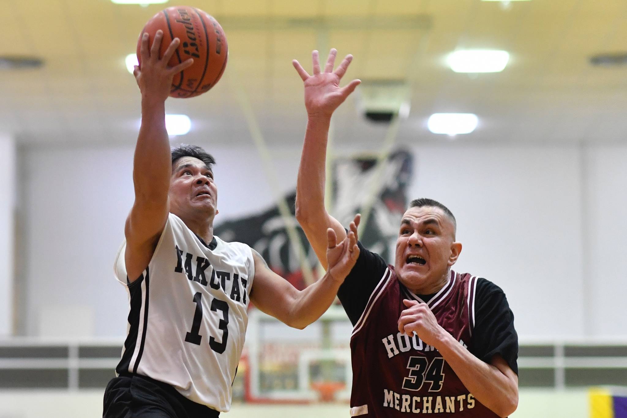 Yakutat’s Jerry Riddlington, left, lays the ball up against Hoonah’s James Mercer in the Masters bracket game at the Gold Medal Basketball Tournament on Thursday, March 21, 2019. (Michael Penn | Juneau Empire)