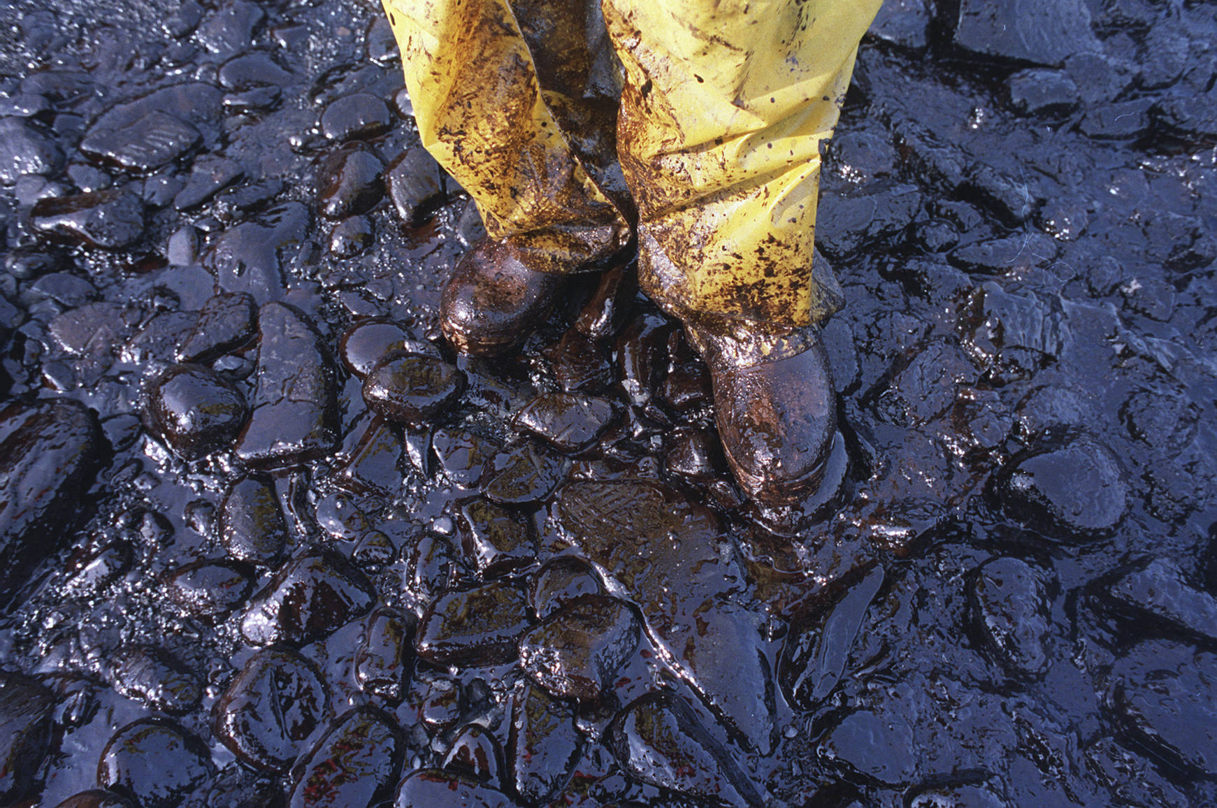 In this April 11, 1989 photo, thick crude oil that washed up on the cobble beach of Evans Island sticks to the boots and pants of a local fisherman in Prince William Sound, Alaska. The Exxon Valdez tanker oil spill on March 24 blackened hundreds of miles of coastline. (John Gaps III | Associated Press File)