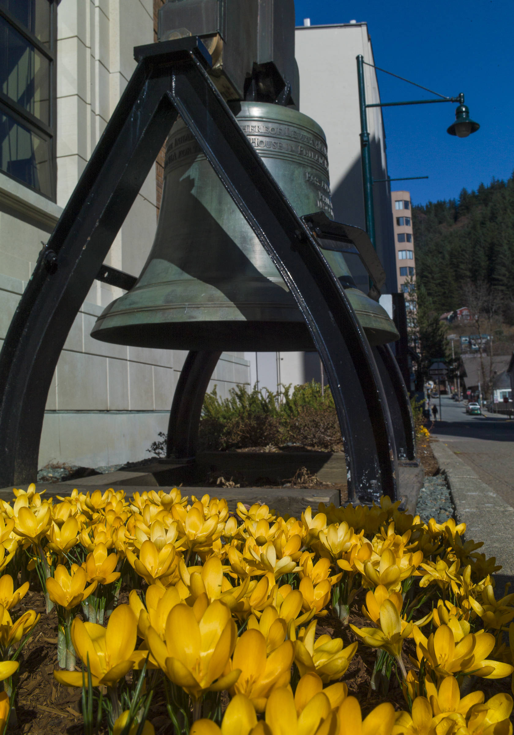 Crocuses pop up near a copy of the Liberty Bell in front of the Alaska State Capitol on Friday, March 29, 2019. (MIchael Penn | Juneau Empire)
