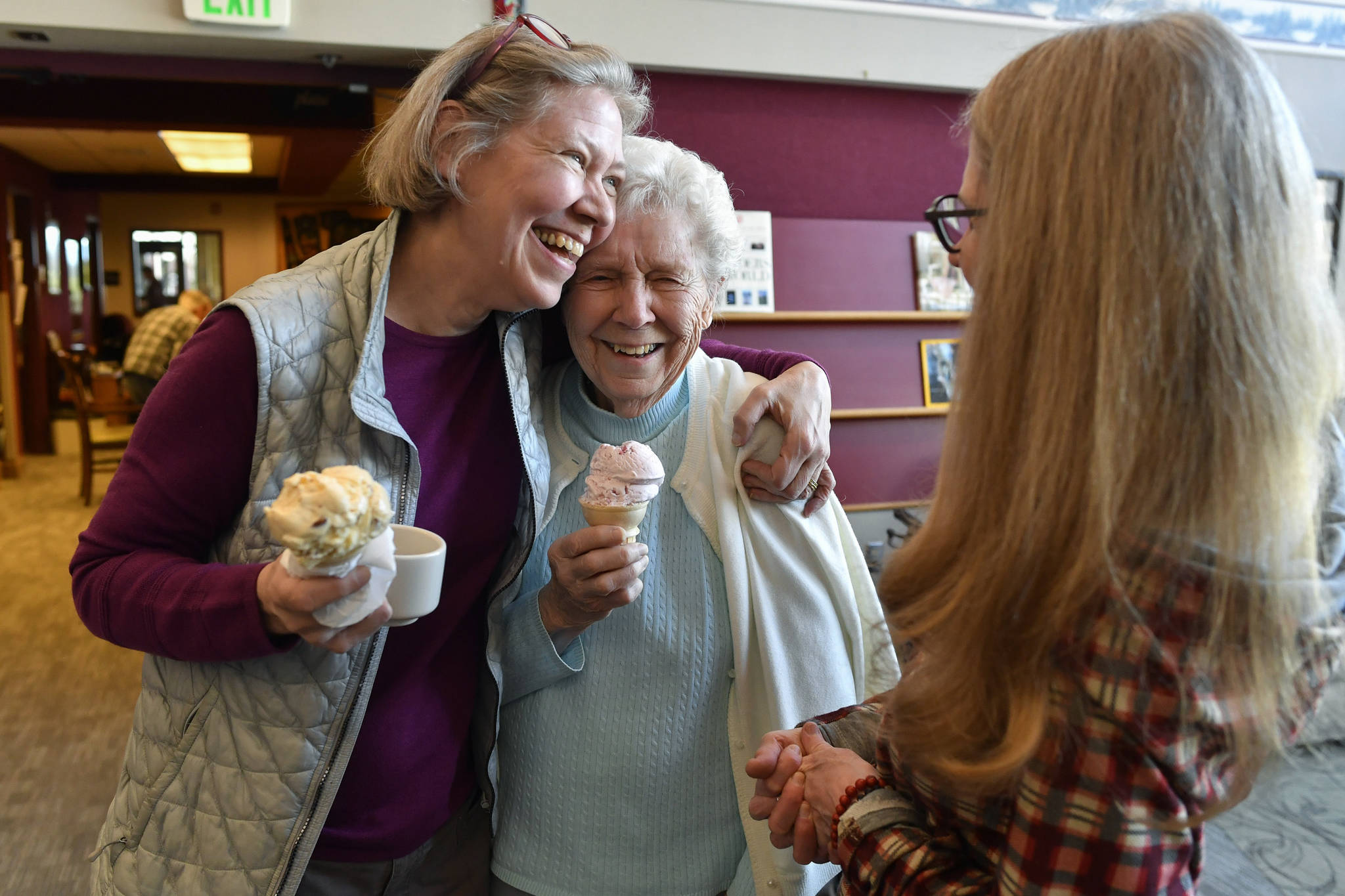 In this March 8, 2019 photo, Margie Beedle, left, hugs her mother, Sally Thibodeau, as they chat with Alaska Pioneer Home employee Laura Minne during the homes weekly ice cream social. (Michael Penn | Juneau Empire File)