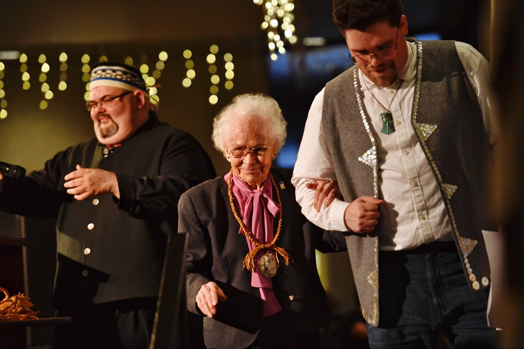 Marie Olson (Kaayistaan) is escorted off the stage by Master of Ceremonies David R. Boxley (Gyibaawm Laxha), right, after she received the President’s Life Achievement Award from Tlingit & Haida President Chalyee Éesh Richard Peterson during the President’s Award Banquet and Language Fundraiser at the Elizabeth Peratrovich Hall on Friday, April 12, 2019. (Michael Penn | Juneau Empire)