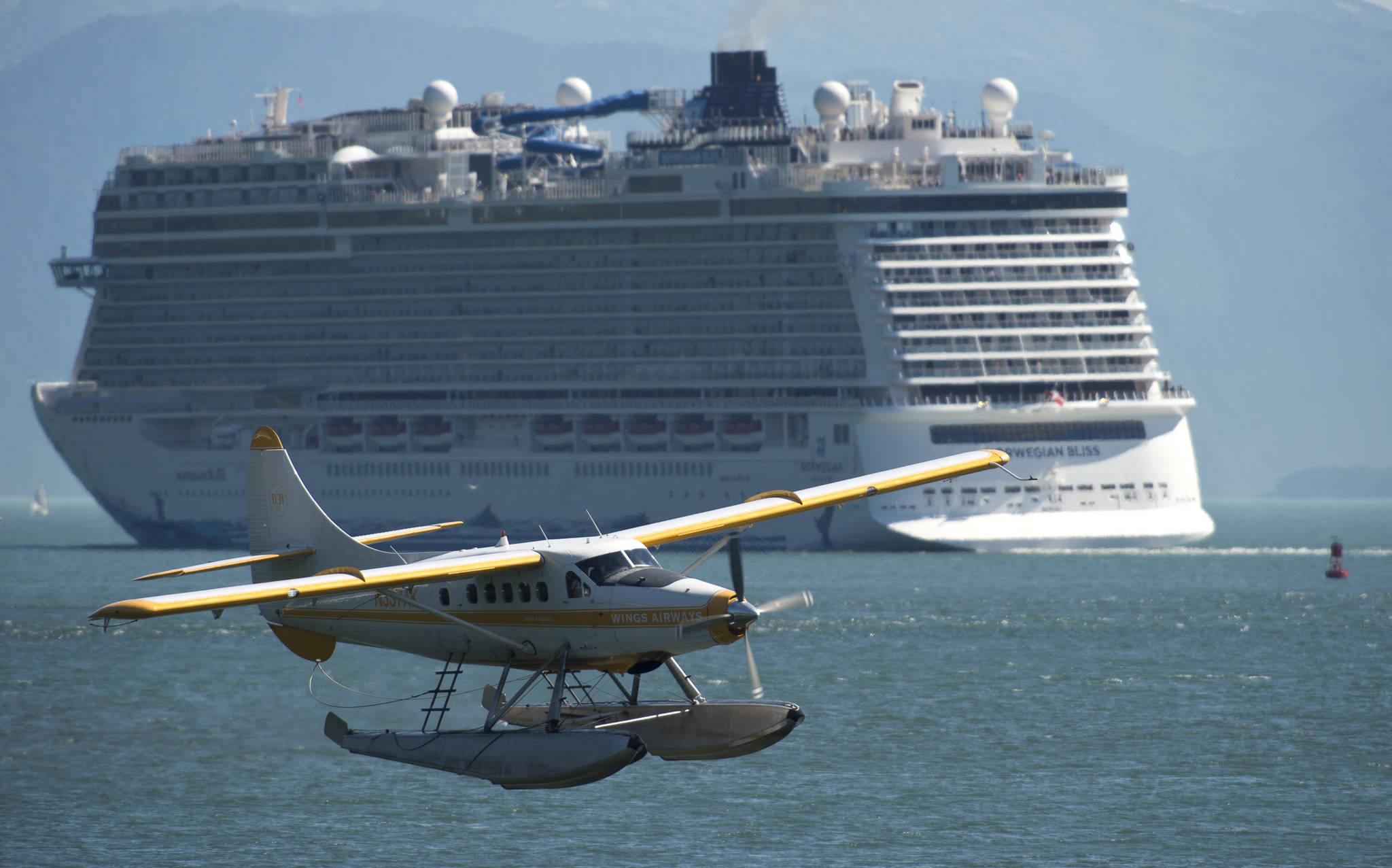 A Wings Airways floatplane takes off from Juneau’s downtown harbor as the Norwegian Bliss leaves its port of call on Tuesday, July 31, 2018. (Michael Penn | Juneau Empire File)