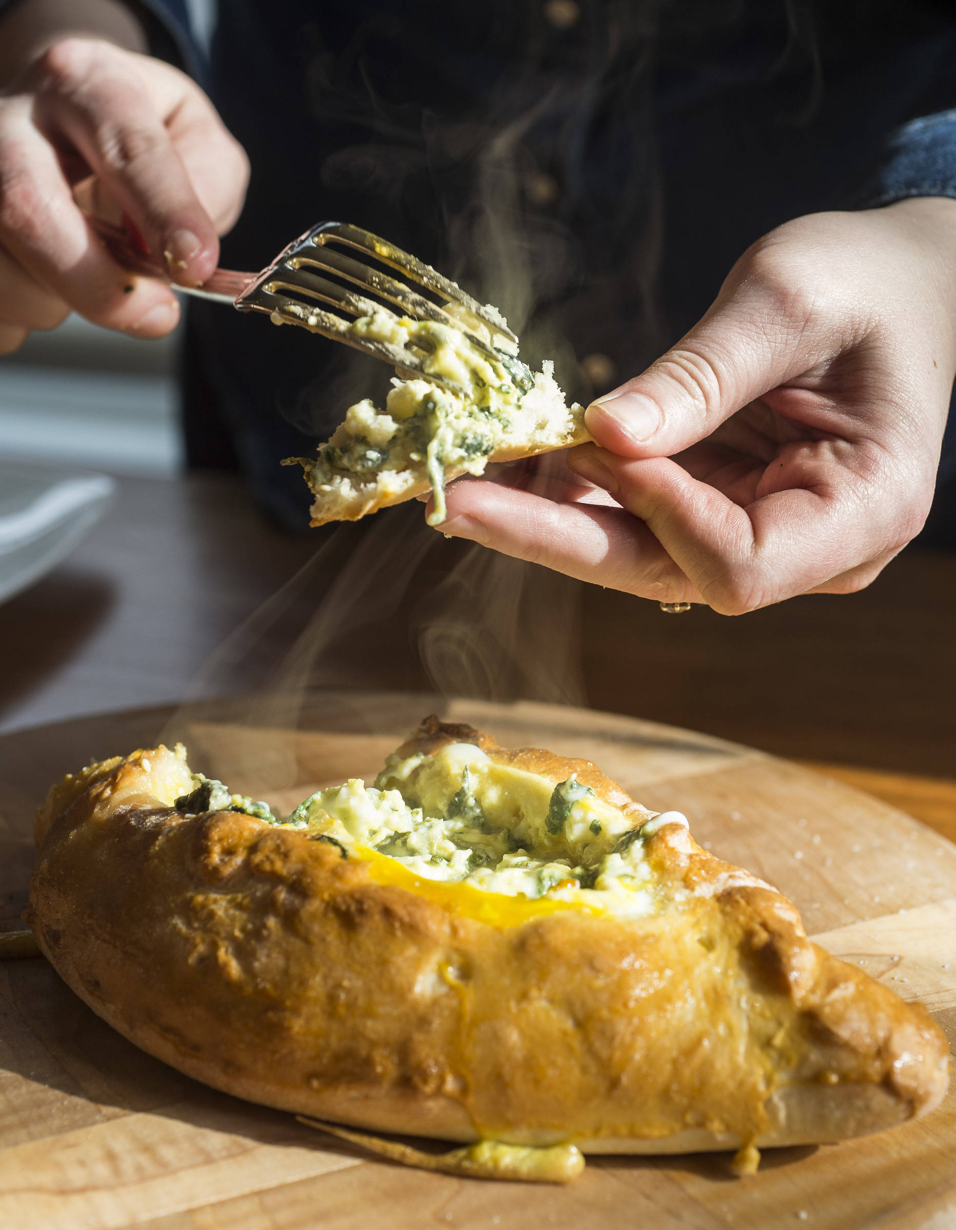 Erin Anais Heist prepares and bakes a khachapuri with nettles, feta and mozzarella cheese and topped with an egg on Friday, April 12, 2019. (Michael Penn | Juneau Empire)