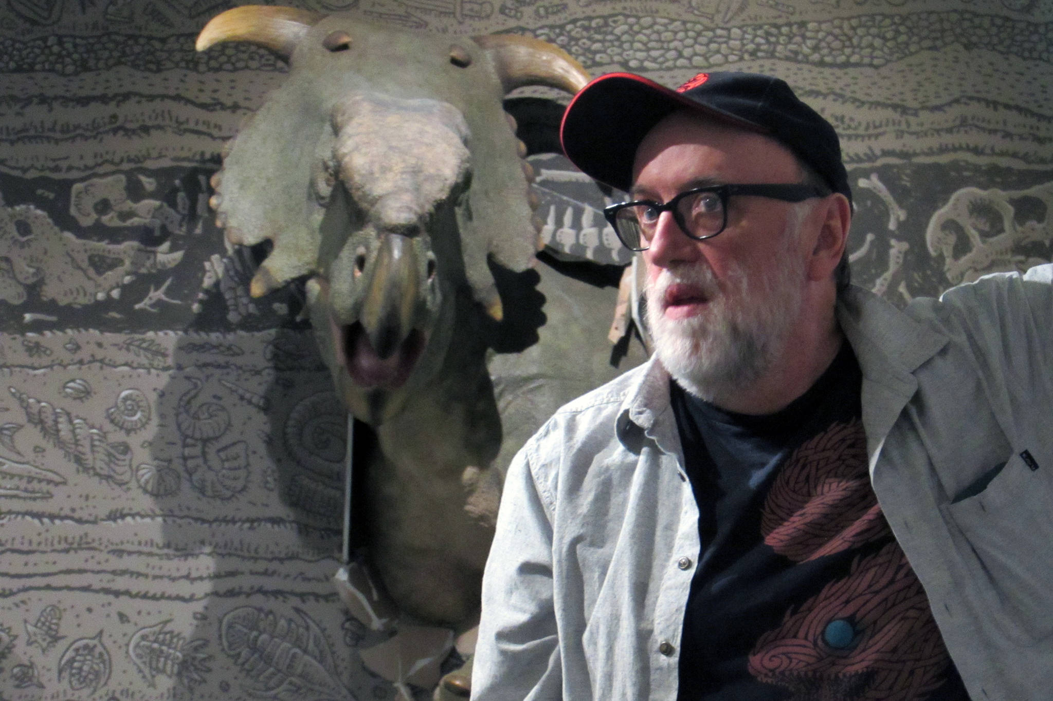 Ray Troll speaks in front of a statue of a pachyrhinosaurus made by Gary Staab on Thursday, May 2, 2019. The statue is part of the “Cruisin’ the Fossil Coastline” exhibition at the Alaska State Museum. (Ben Hohenstatt | Juneau Empire)
