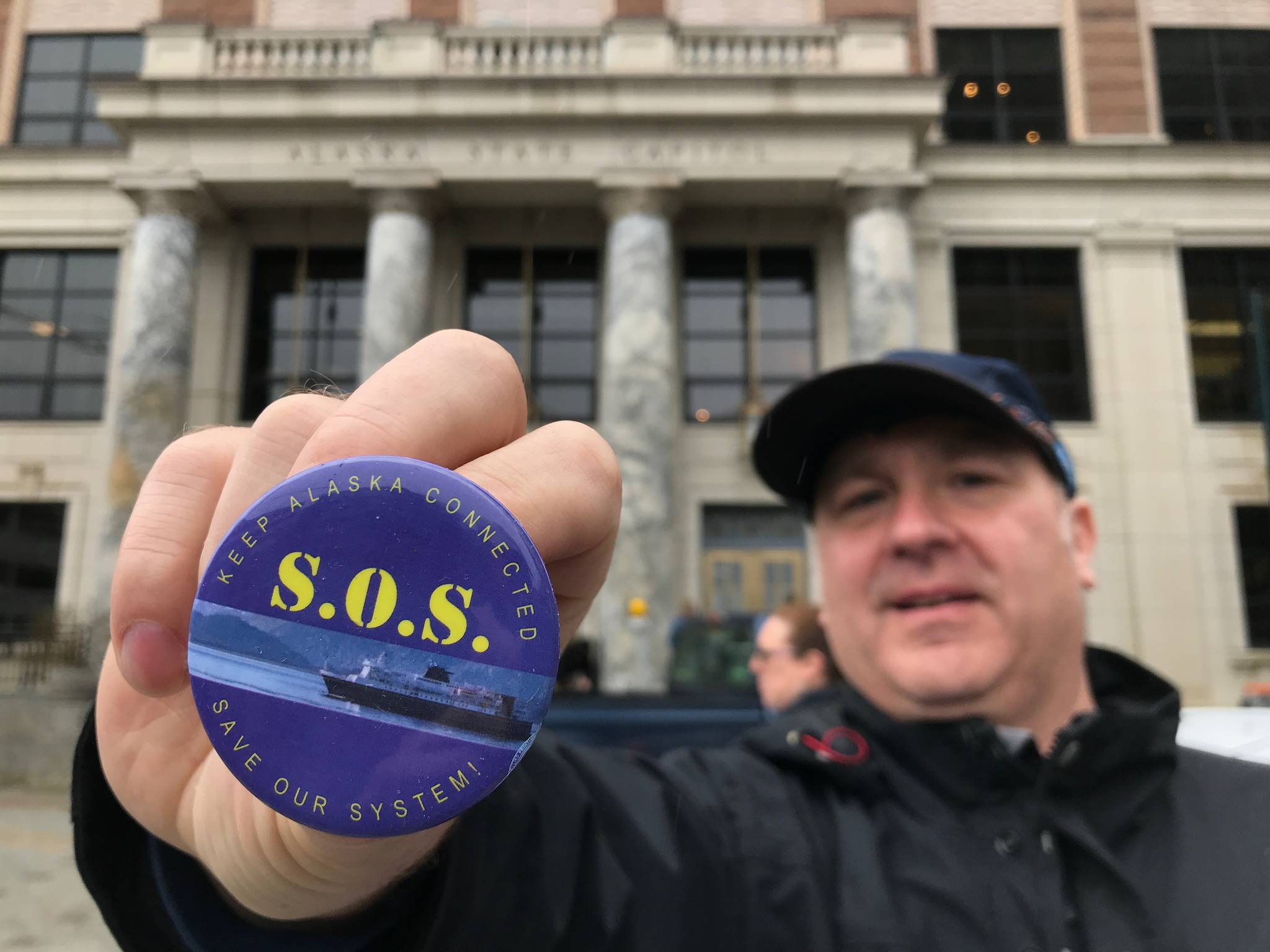 Drew Transkei, of Ketchikan, holds up a pin before a SOS Rally at the Capitol on Tuesday, May 7, 2019. (Michael Penn | Juneau Empire)