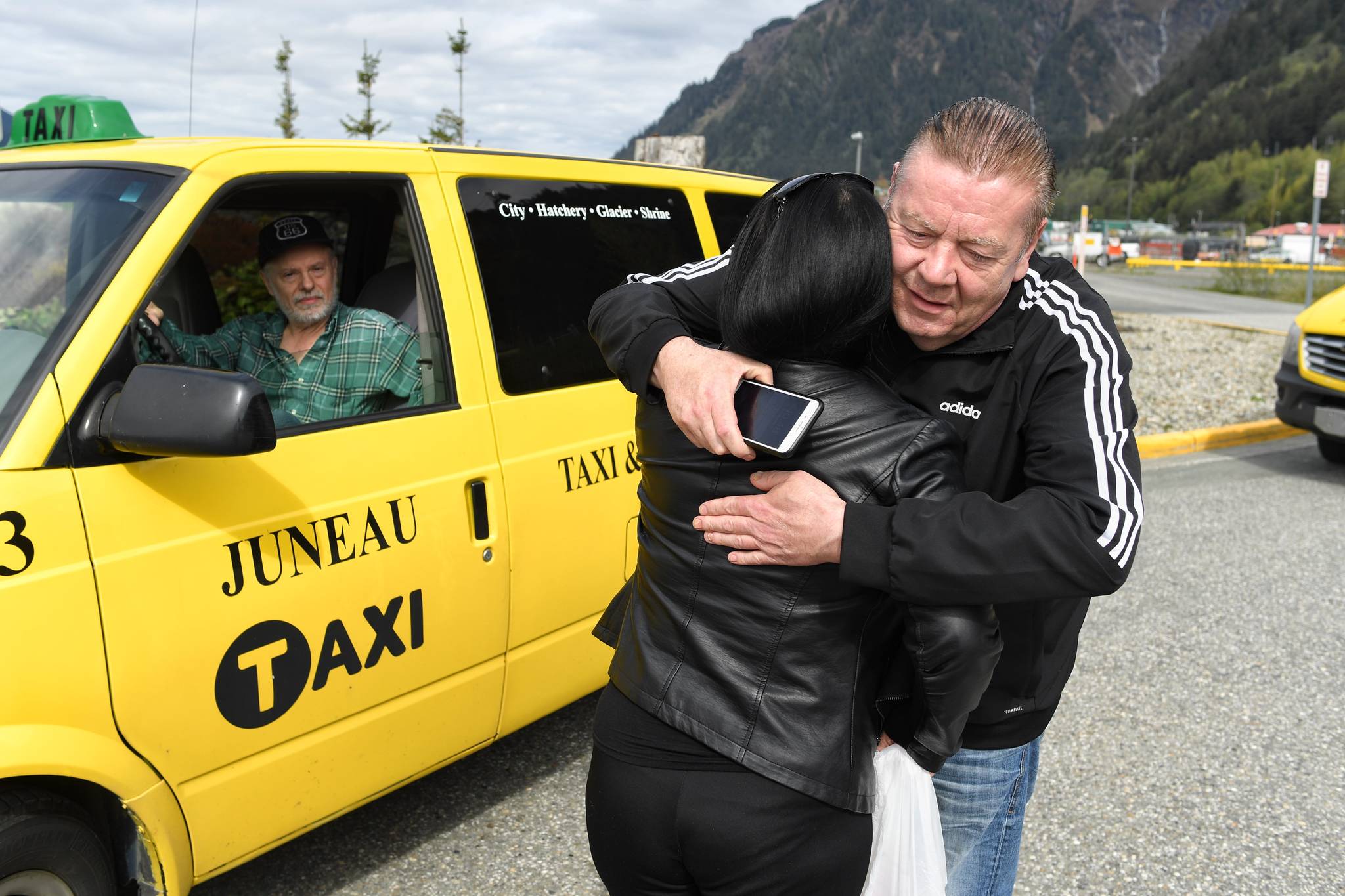 Taxi driver George O’Malley gives Monica Campbell a hug as Tony Schandler looks on before Juneau taxi drivers parade through downtown Juneau in honor of Scott Campbell on Friday, May 10, 2019. (Michael Penn | Juneau Empire)
