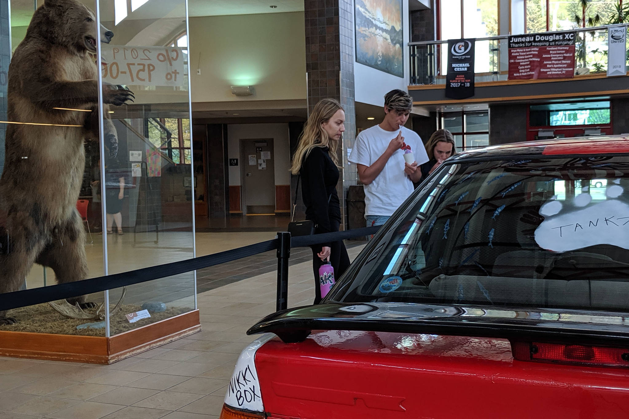 Senior Anna Kahklen pauses with senior Cassious English and freshman Kylah Bentz to admire a car located in the Juneau-Douglas High School: Yadaa.at Kalé commons. (Ben Hohenstatt | Juneau Empire)