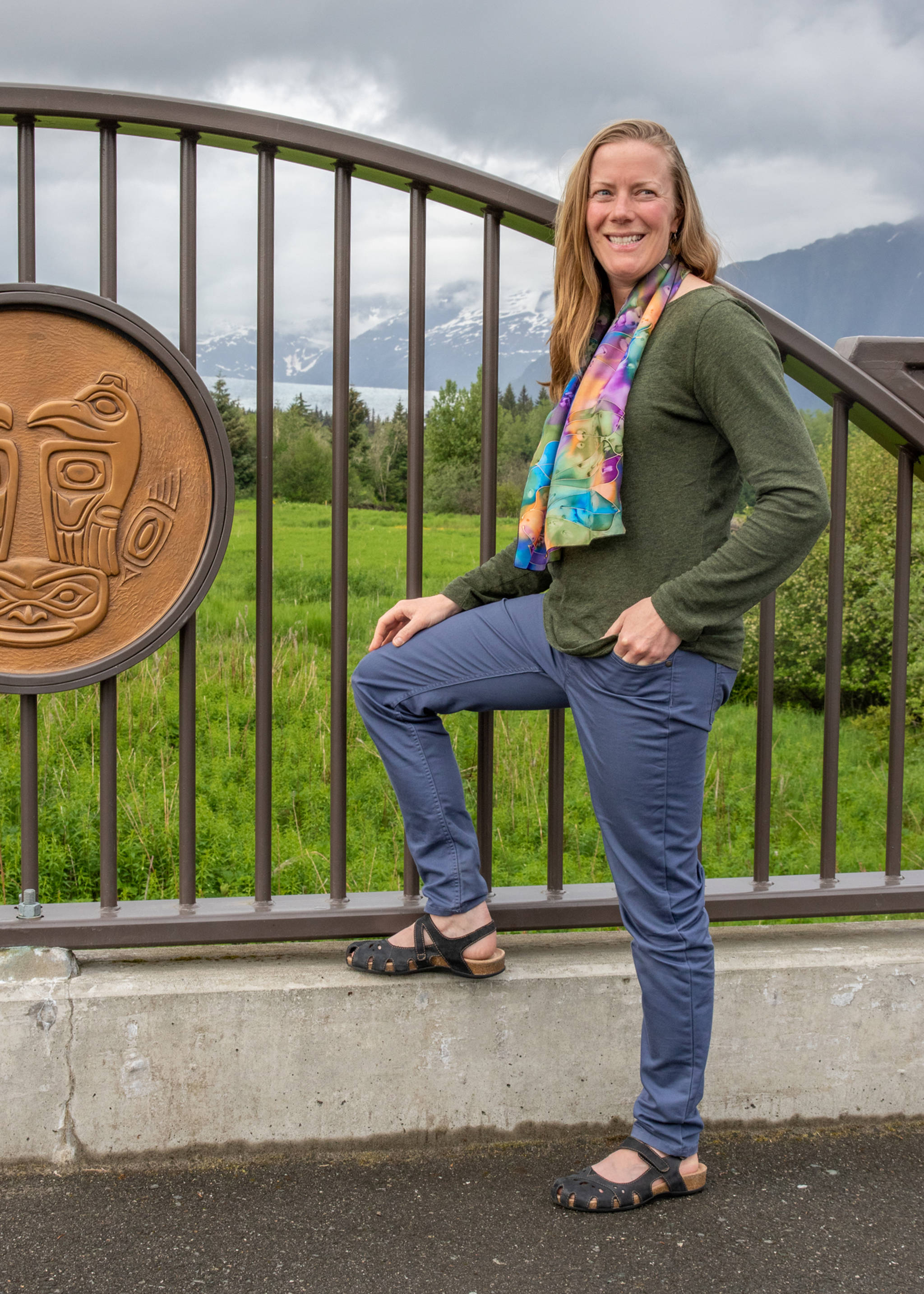 June 9, 2019: Laura Baker has a style that goes straight from work to play. A physical therapist, she wears clothes that support a professional and active lifestyle. She is wearing a heather green pullover from J. Crew, slate blue trousers from Patagonia and black sandals from Earth Origins. Her accessories include a multi-colored silk scarf from Tasmania and earrings by Juneau artist, Julienne Pacheco, WILD by Nature. (Kerry Howard | For the Juneau Empire)