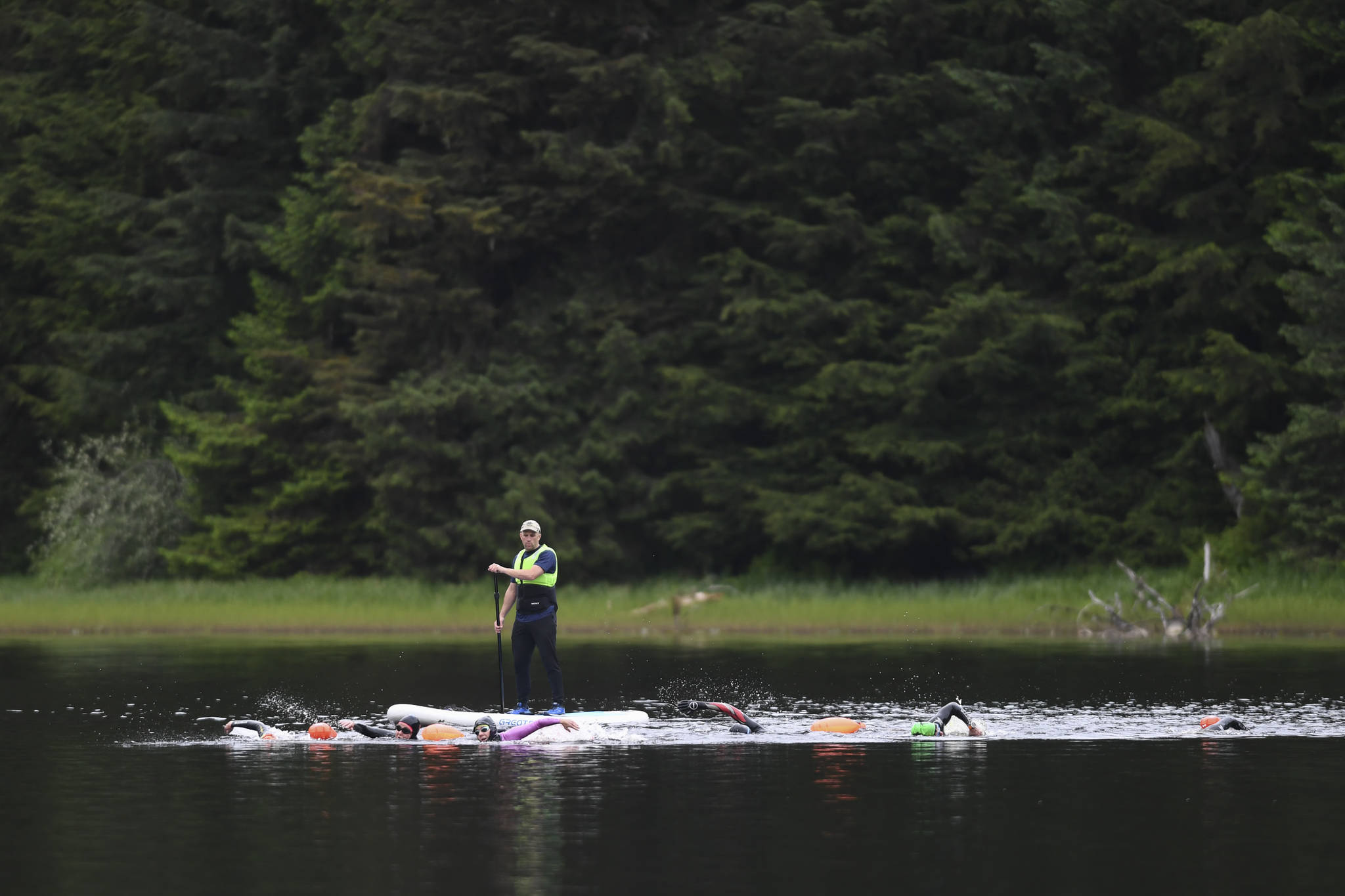 Kevin Sellers follows along on a standup paddle board as swimmers train in Auke Lake on Wednesday, June 5, 2019. (Michael Penn | Juneau Empire)