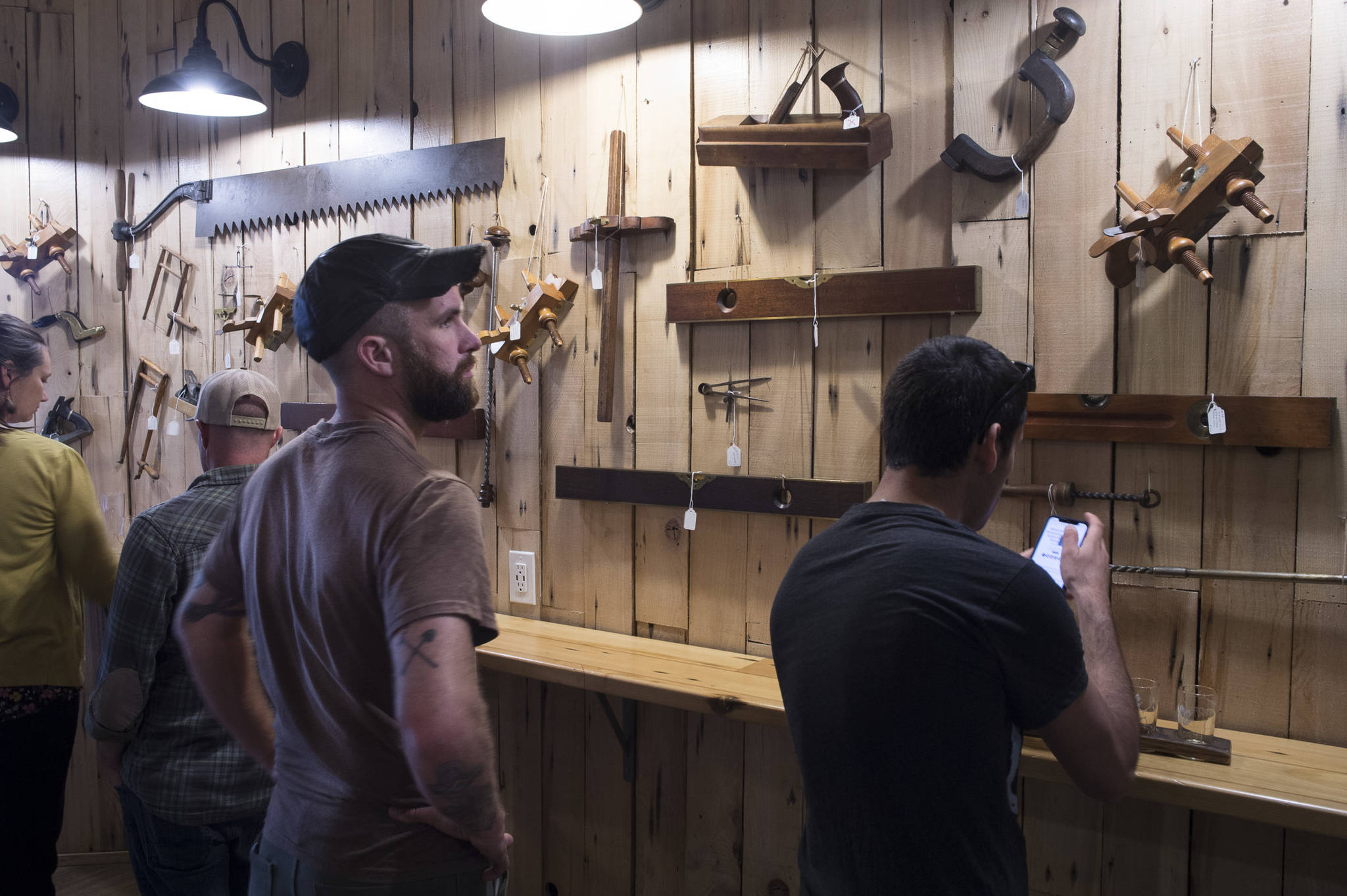 Ryan OShaughnessy studies the collection of antique woodworking tools collected by Dick Wood during First Friday at Devils Club Brewing Company on Friday, June 7, 2019. (Michael Penn | Juneau Empire)