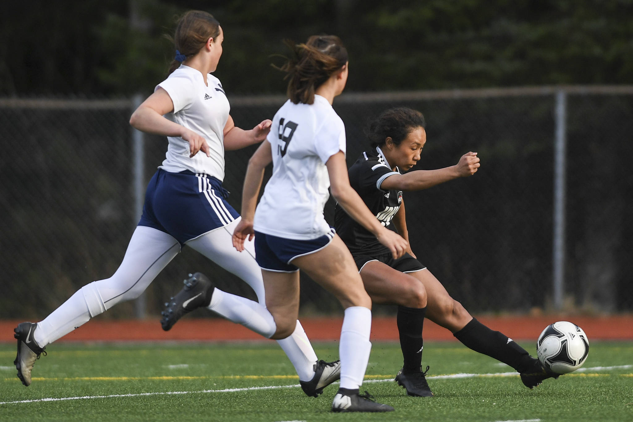 Juneau-Douglas’ Malia Miller, right, shoots and scores against Soldotna’s Sierra Longfellow, left, and Caleigh Glassmaker at Adair-Kennedy Memorial Field on Friday, April 26, 2019. JDHS won 4-0. (Michael Penn | Juneau Empire)