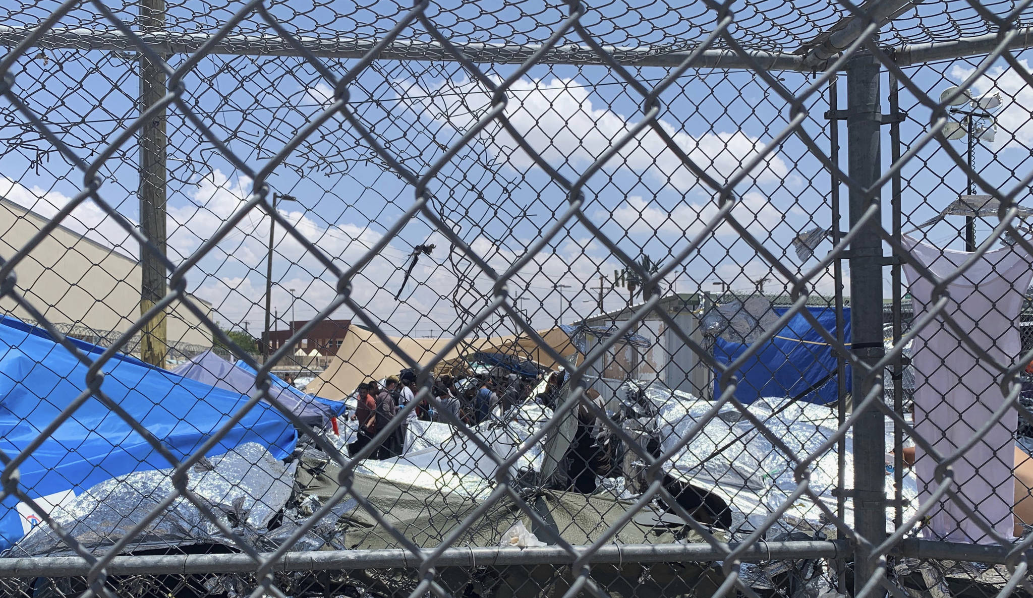 In this June 1, 2019, photo, provided by New Mexico State University professor Neal Rosendorf, migrants are seen through fencing inside a temporary outdoor encampment where they’re waiting to be processed in El Paso, Texas. Rosendorf said it resembled a “human dog pound.” (Neal Rosendorf via AP)