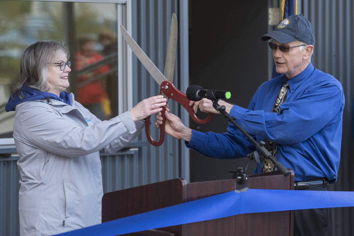 Port Director Carl Uchytil hands oversized scissors toTravel Juneau President & CEO Liz Perry during a ceremony to open the new Visitor’s Center Kiosk, Friday, May 17, 2019. Uchytil is talking to the Greater Juneau Chamber of Commerce today. (Michael Penn | Juneau Empire)
