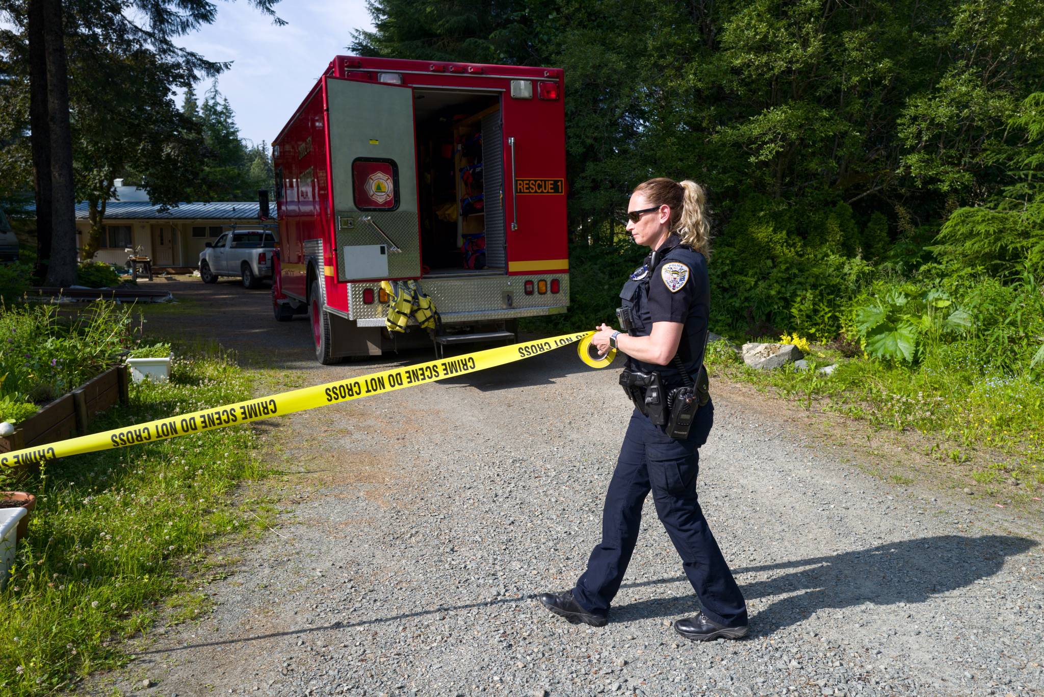 JPD Officer Mattie Shriver put up police tape at 9010 Atlin on Wednesday, July 3, 2019. A body was reportedly found in a pond behind the house. (Michael Penn | Juneau Empire)