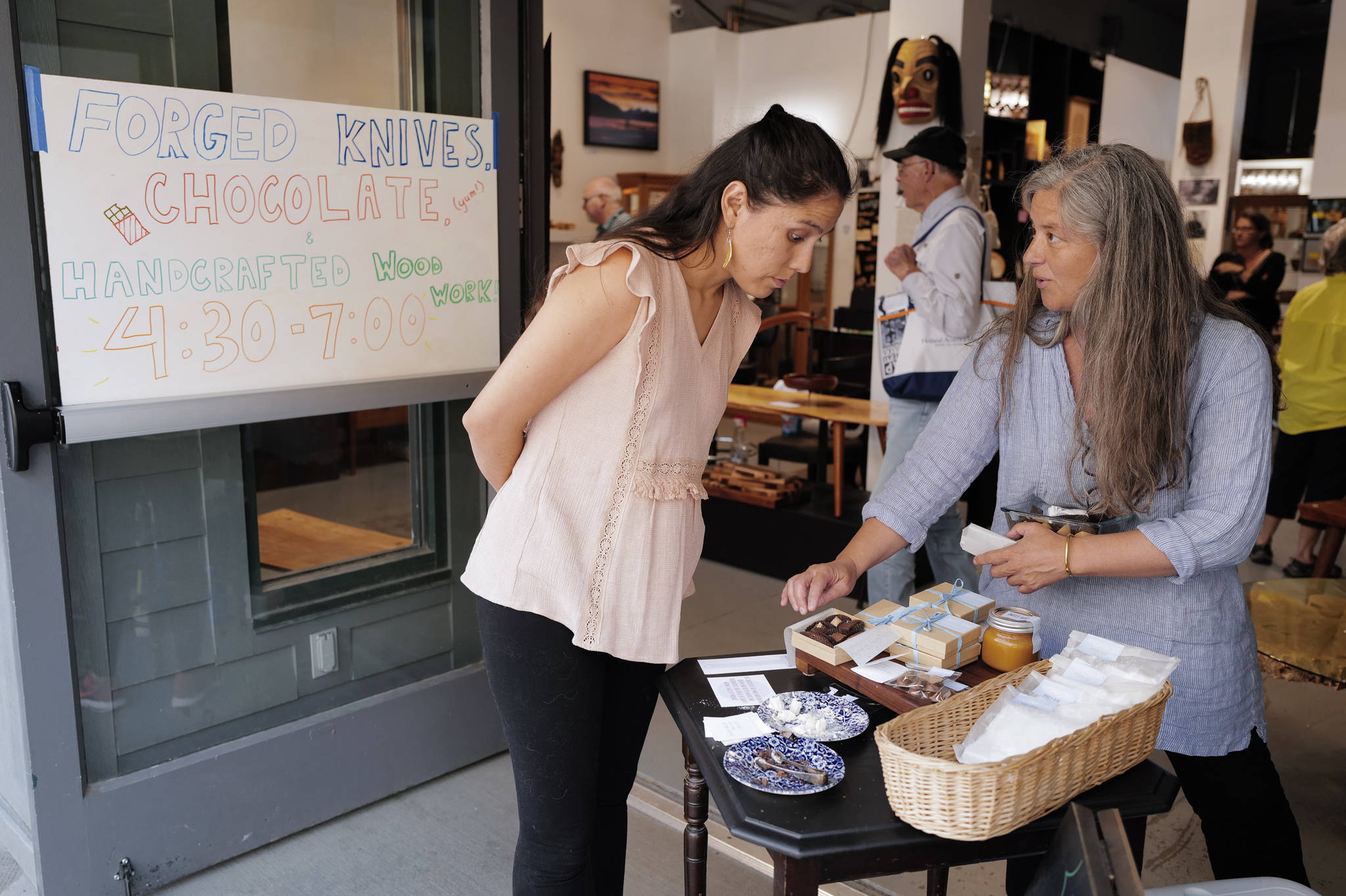 Marta Lastufka, right, owner of Sweet Song Chocolates, shows her wares to Elia Salinas during First Friday at Rainforest Designs on South Franklin Street on Friday, July 5, 2019. Lastufka was one of three featured artists at the local artisans shop. Wood worker Henry Webb and knife maker Liam Penn were also featured. (Michael Penn | Juneau Empire)