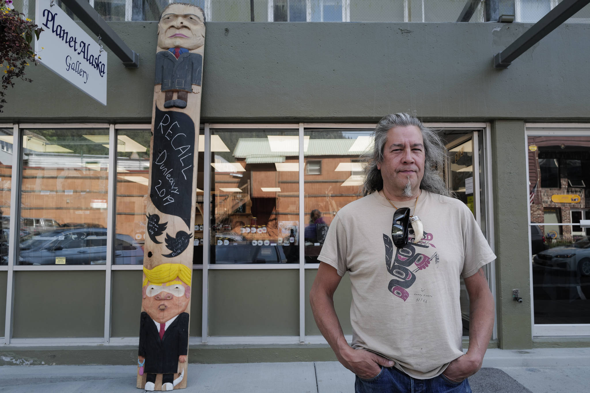 Sitka artist Tommy Joseph stands with the ridicule pole he carved in front of the Planet Alaska Gallery on Ferry Way on Wednesday, July 31, 2019. The pole includes likenesses of Alaska Gov. Mike Dunleavy, top, and President Donald Trump. (Michael Penn | Juneau Empire)