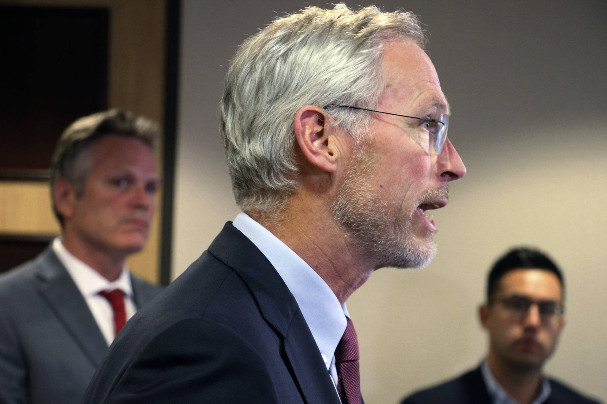 University of Alaska President Jim Johnsen speaks at a news conference in Anchorage, Alaska, Tuesday, Aug. 13, 2019, where Gov. Mike Dunleavy, back left, announced he would support a $25 million cut this year to the University of Alaska system. That is a sharp reversal from the $135 million cut Dunleavy earlier endorsed. In background at right is Dunleavy’s spokesman Matt Shuckerow. (AP Photo/Mark Thiessen)