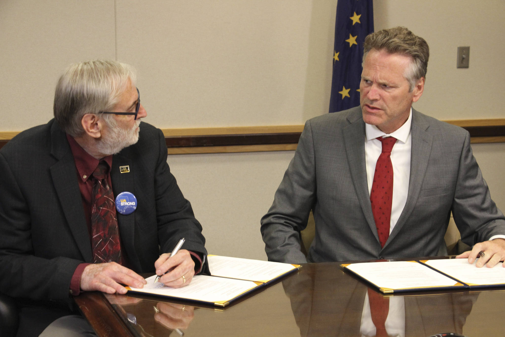 University of Alaska Board of Regents chairman John Davies, left, and Gov. Mike Dunleavy sign an agreement, Tuesday, Aug. 13, 2019, in Anchorage, Alaska, that will spread $70 million in cuts to the university system over three years. That is a sharp reversal from the $135 million cut Dunleavy earlier proposed for this year. (AP Photo/Mark Thiessen)