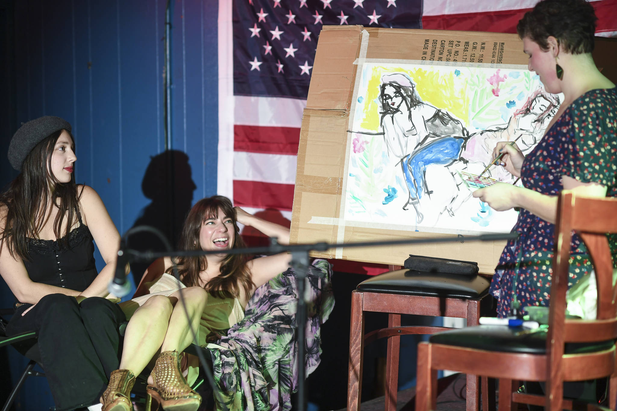 Natalie Weinberg, right, performs with a live model painting of Dana Herndon, center, and Serena Drazkowski during the GRLZ open mic night at the The Rendezvous Bar on Wednesday, Aug. 14, 2019. (Michael Penn | Juneau Empire)
