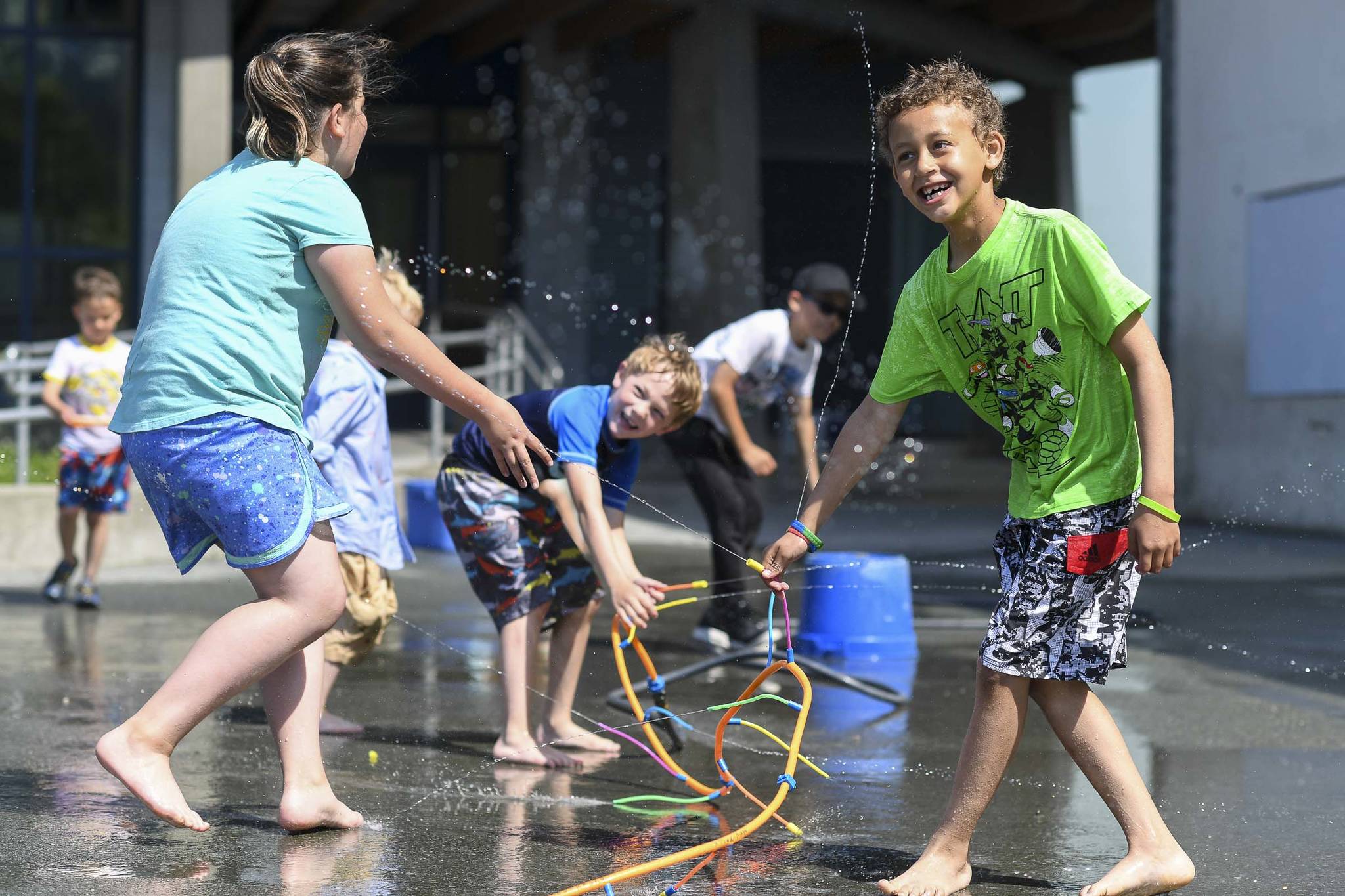 David Kimbrough, 7, right, Clayton Haywood, 6, center, and Kyla Belcourt, 8, play in sprinklers set up during the RALLY program at Harborview Elementary School on Wednesday, June 26, 2019. (Michael Penn | Juneau Empire)