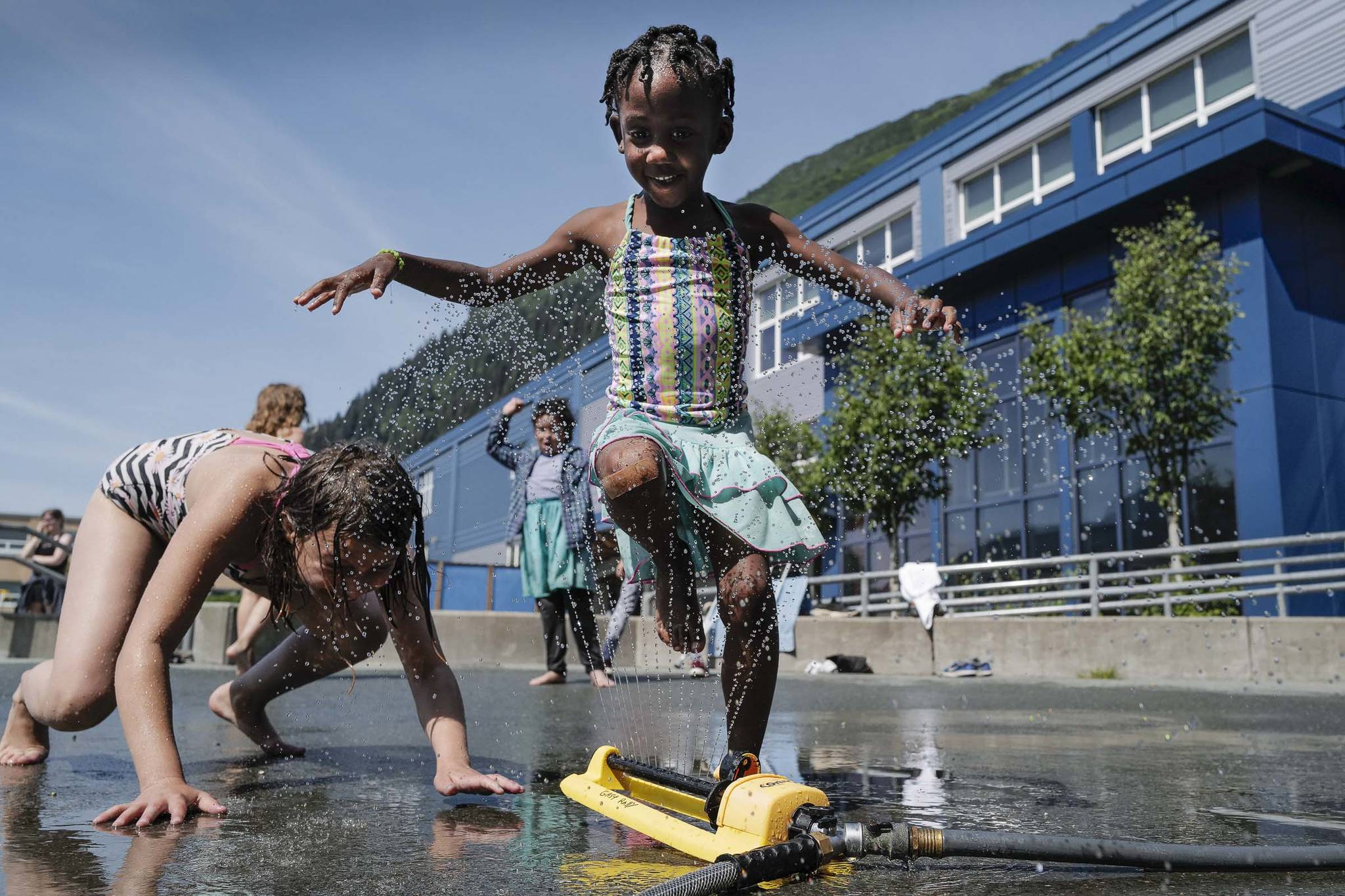 Dallas Hamblin, 5, and Neveah Berryhill, 9, left, play in a sprinkler set up during the RALLY program at Harborview Elementary School on Wednesday, June 26, 2019. (Michael Penn | Juneau Empire)